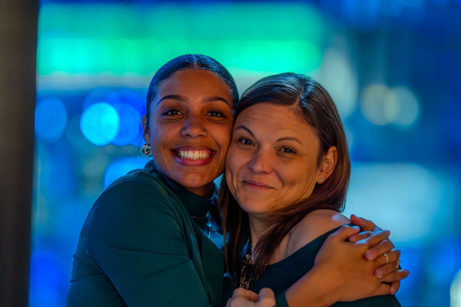 Two women smiling and hugging each other against a colorful bokeh background.