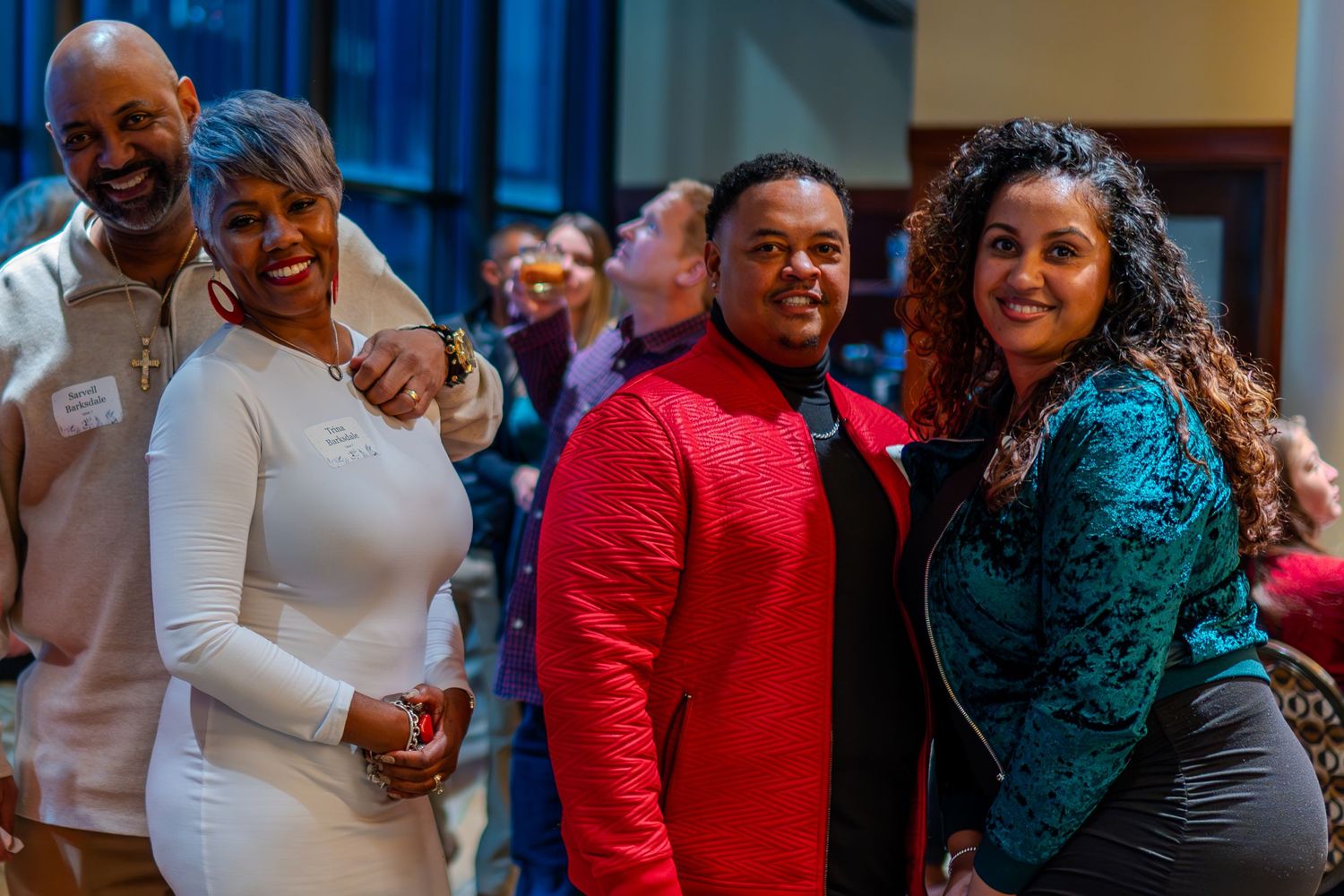 Group of four smiling adults dressed in elegant attire posing together at a social gathering event.