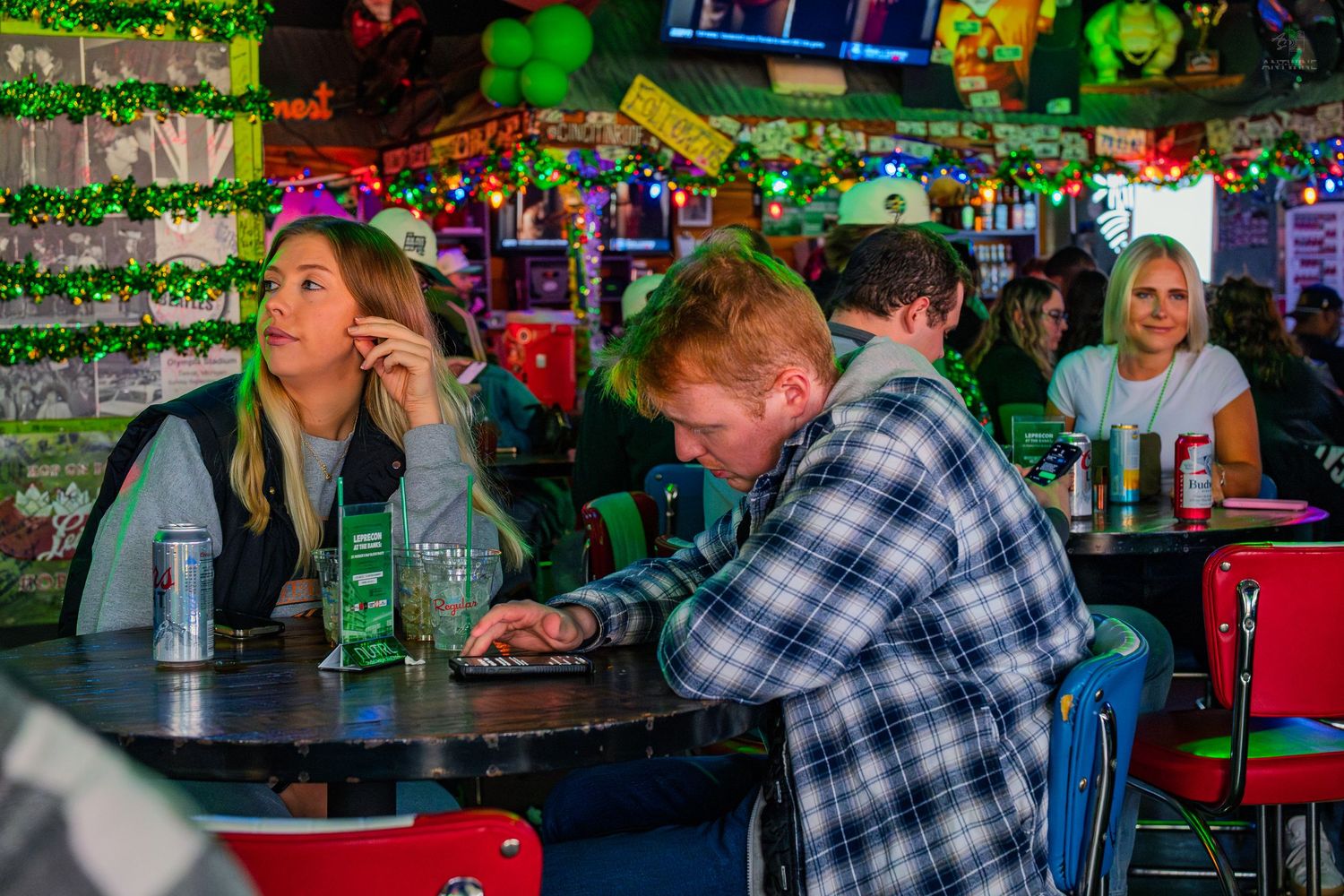 People socializing at a colorful bar with festive decorations, string lights, and drinks on the counter.