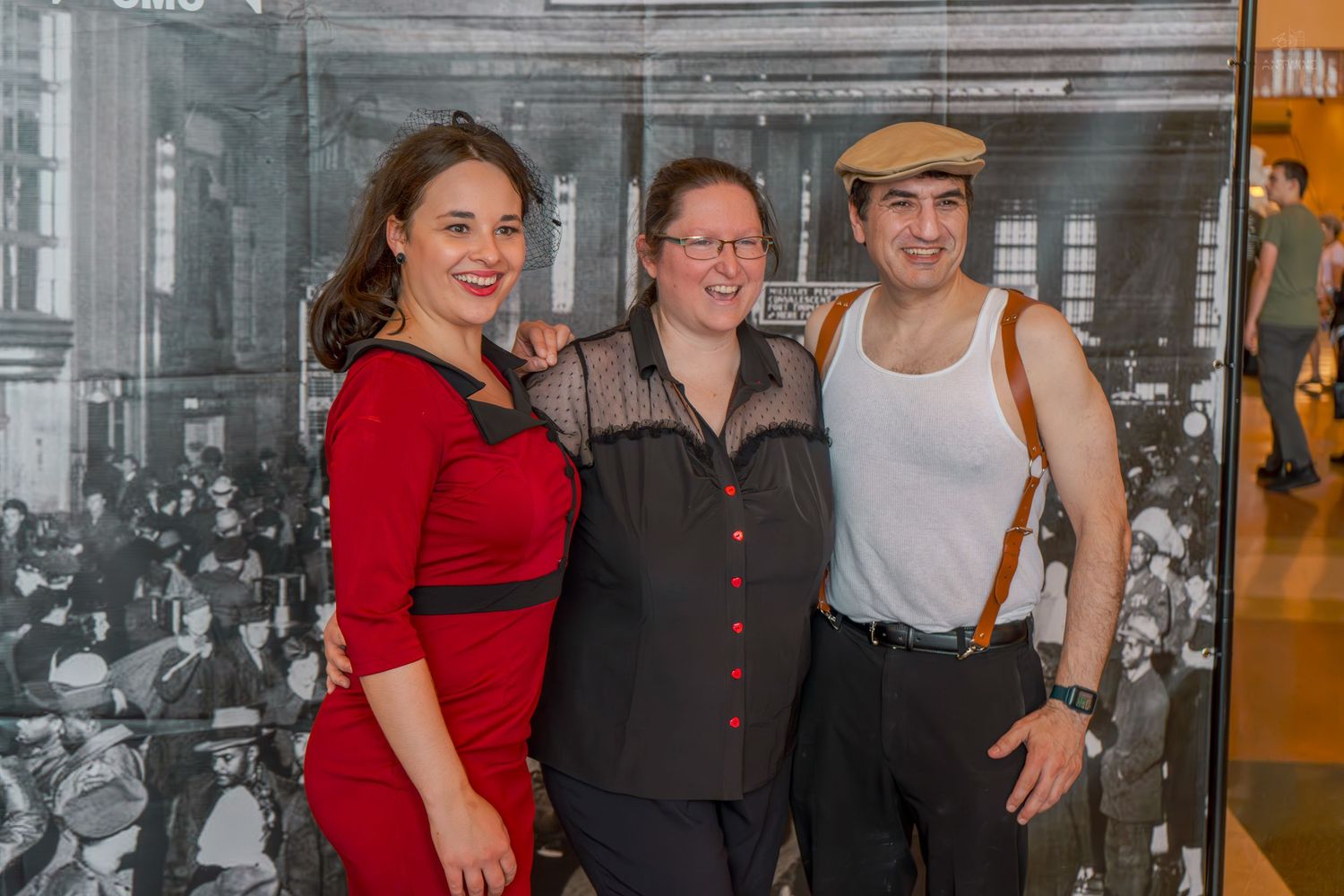 Three people posing together in vintage 1940s-style outfits in front of a black and white historical photo backdrop.