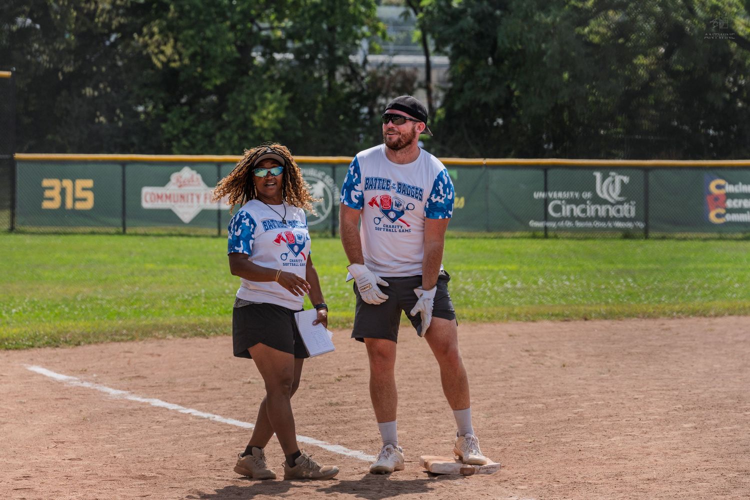Male and female softball players standing together on base during an outdoor charity game.