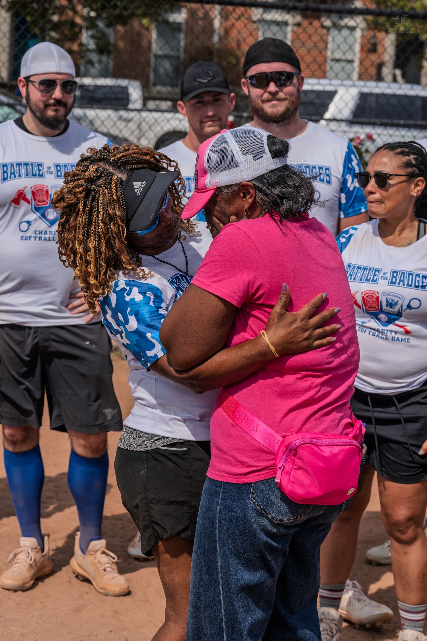 Two women share a warm hug at a Battle of the Badges charity softball game event outdoors.