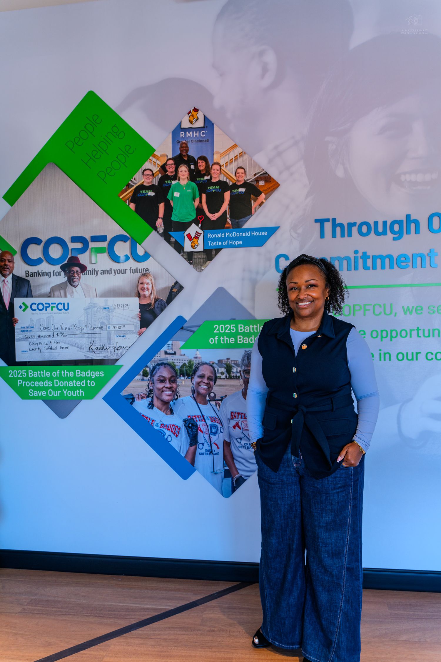 A smiling woman stands in front of a COPFCU credit union promotional banner at a community event.
