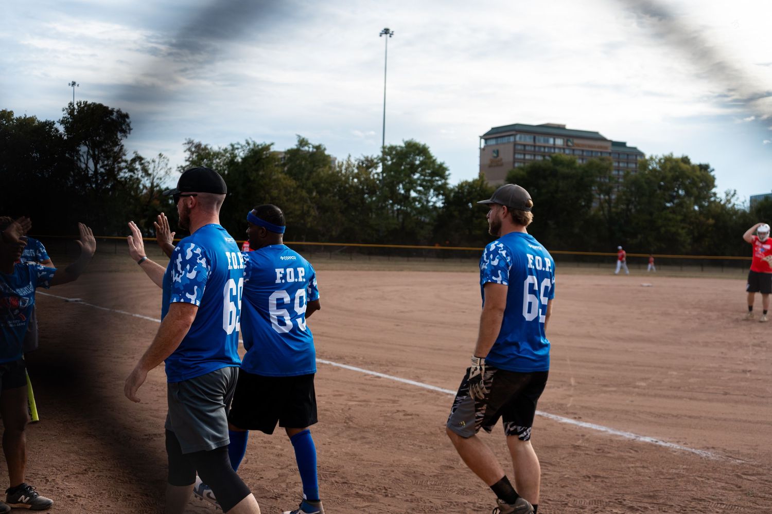 Baseball players in blue uniforms numbered 69 walking on a dirt softball field during a game.
