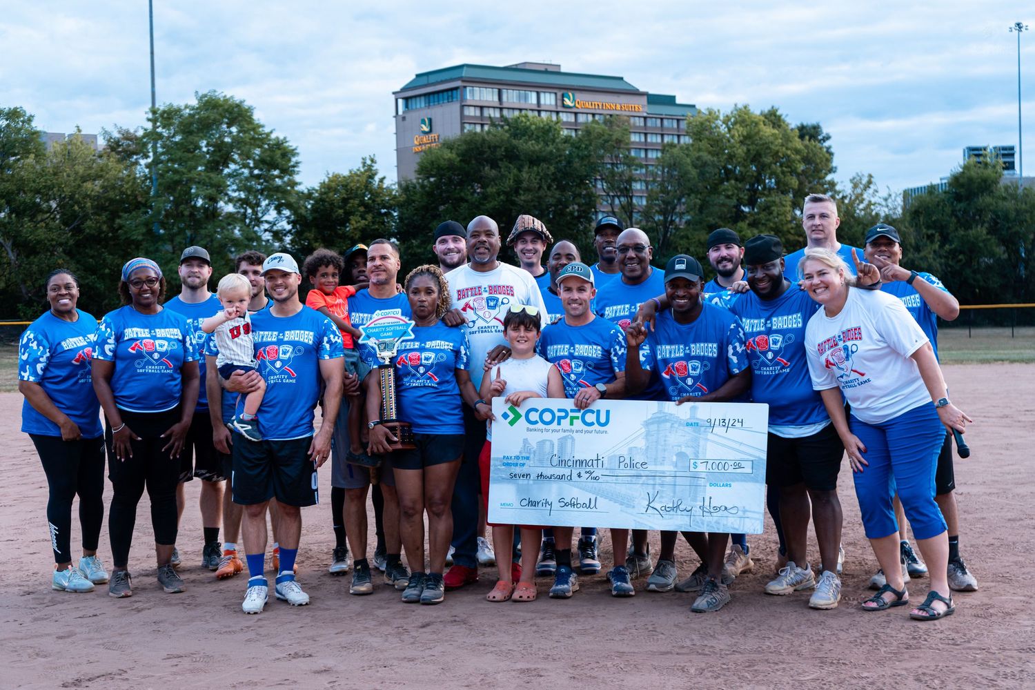 Large group of softball players pose with a COPFCU charity check after a fundraising game.