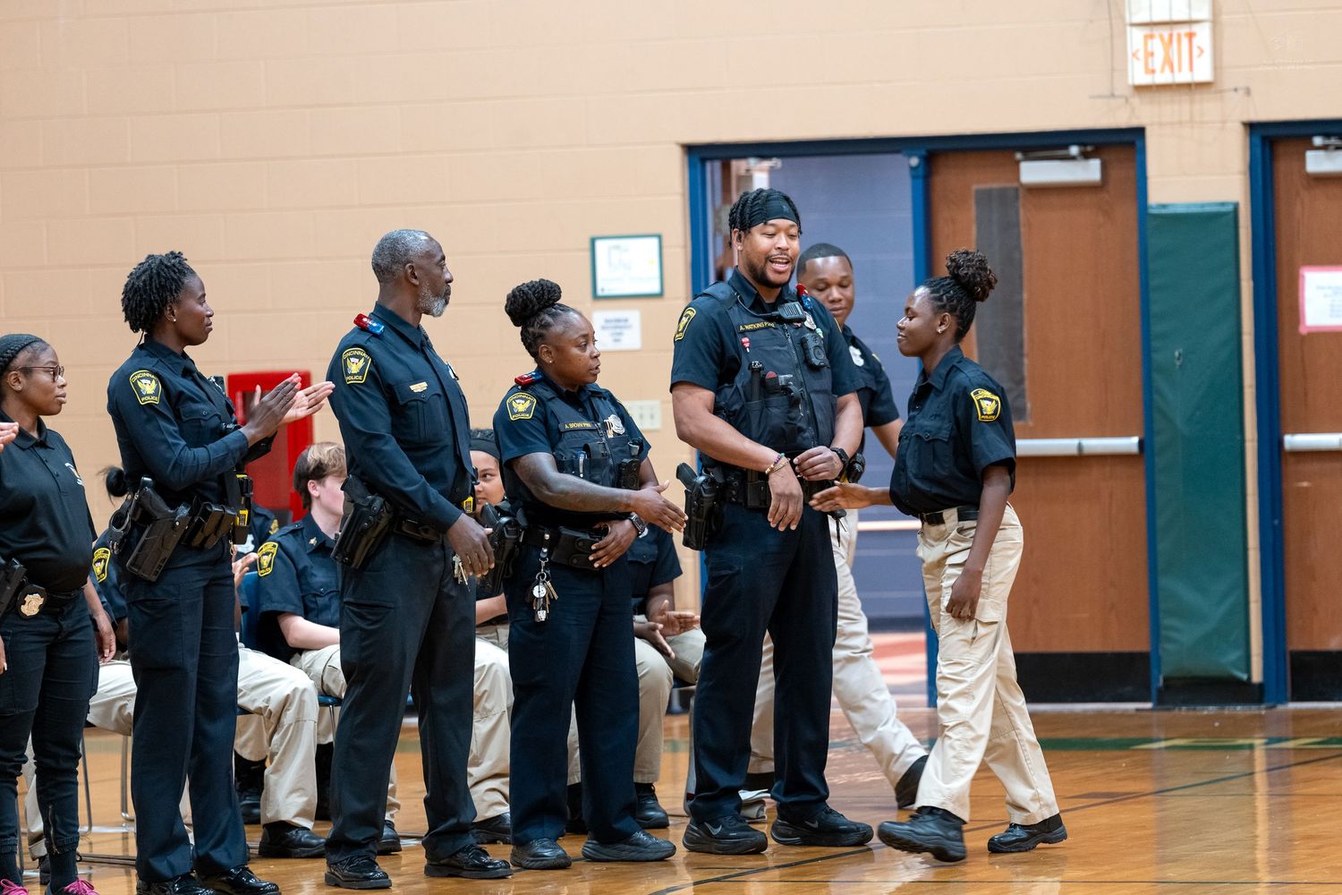 Young students in black uniforms stand in a school gymnasium during a law enforcement youth program ceremony.