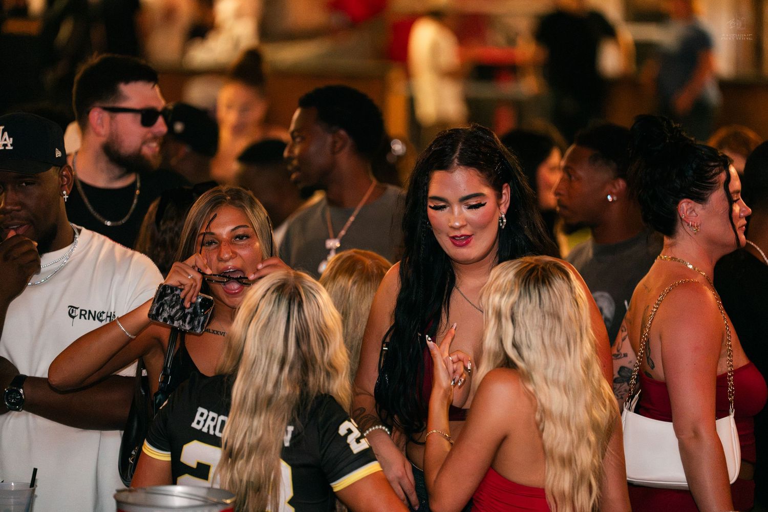 Group of young women in sports jerseys socializing at a busy nightclub bar event.