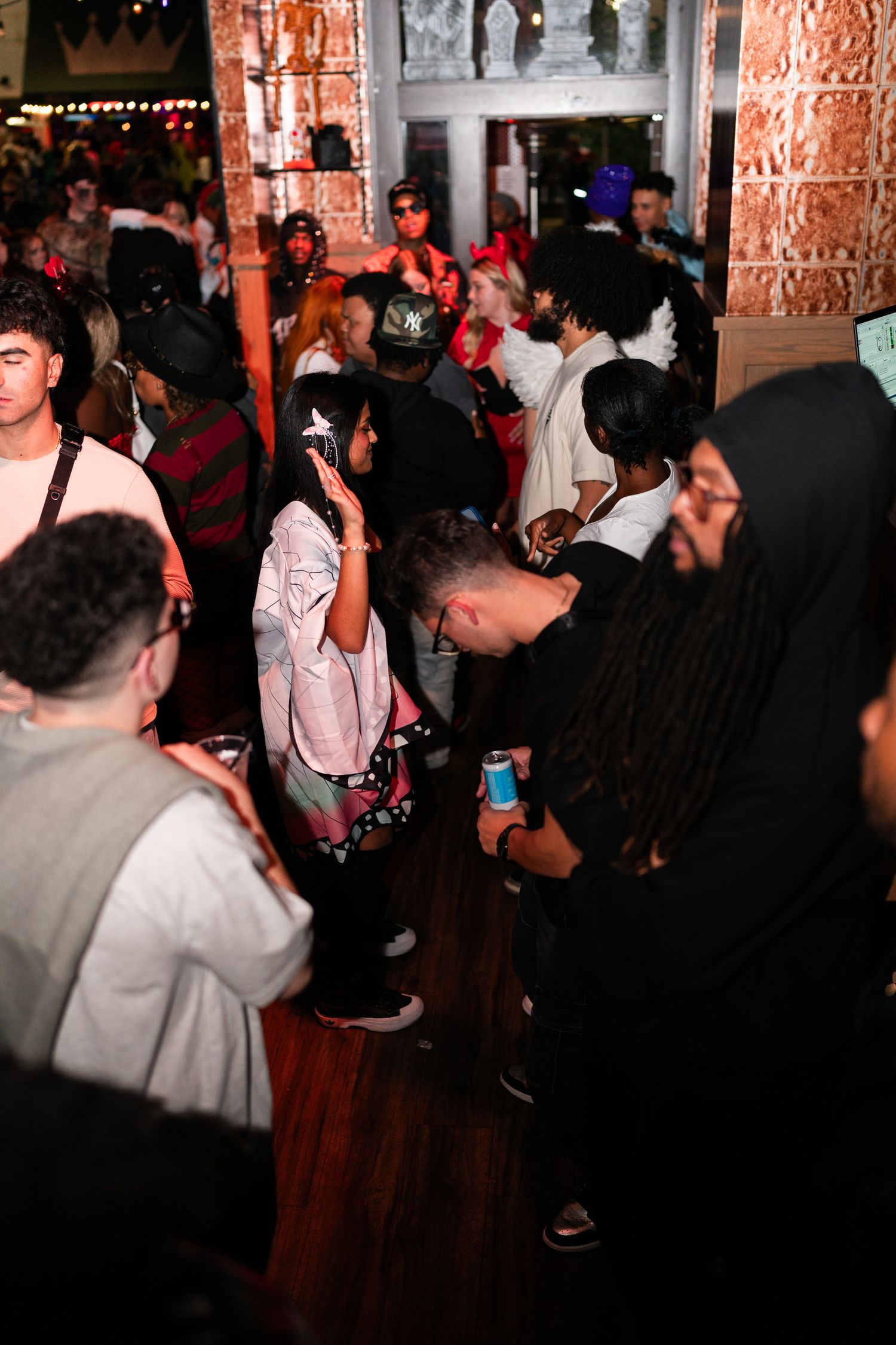 Diverse group of partygoers mingling and dancing inside a lively crowded bar during a Halloween event.