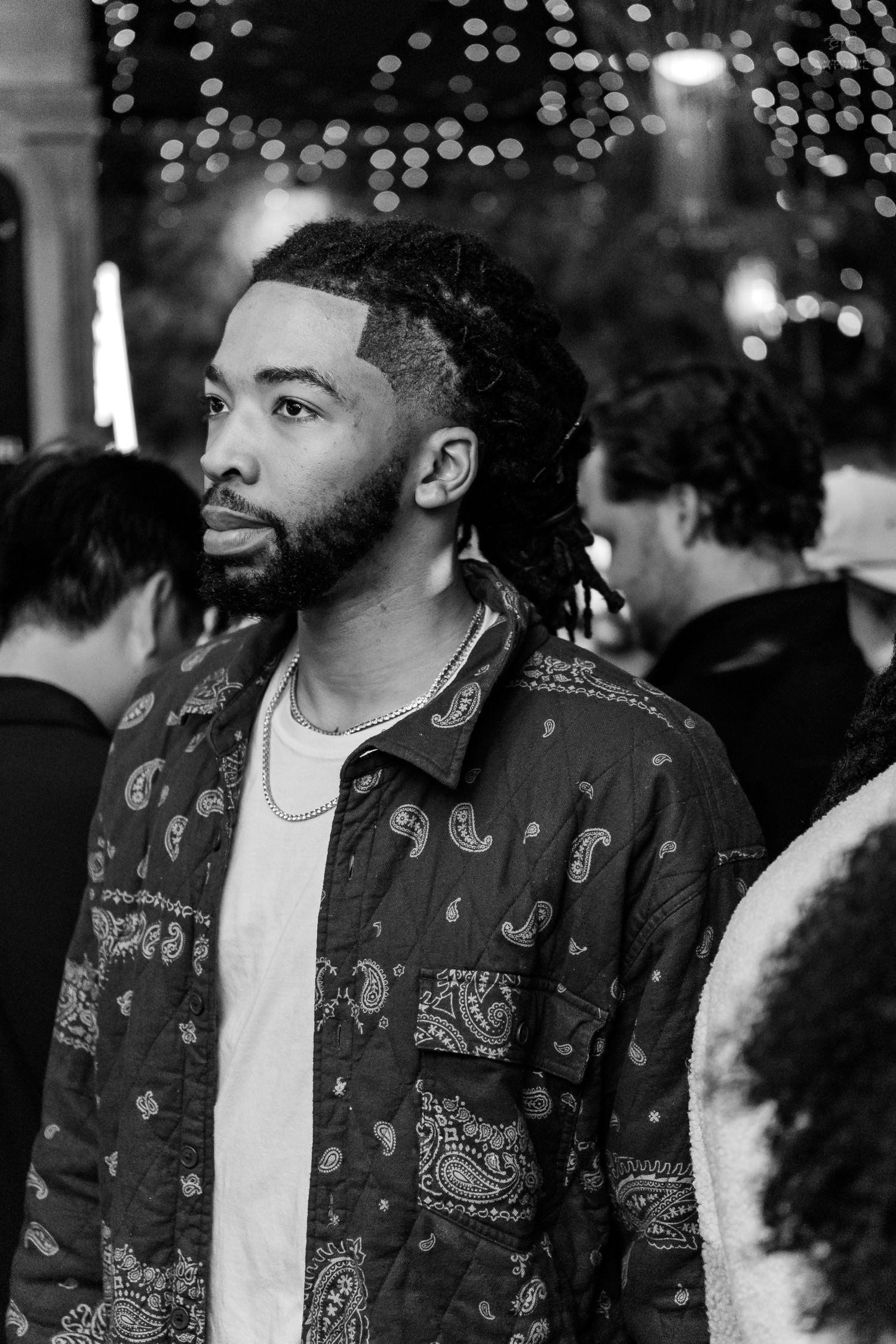 Young man with dreadlocks wearing a paisley shirt at a nightclub gathering.