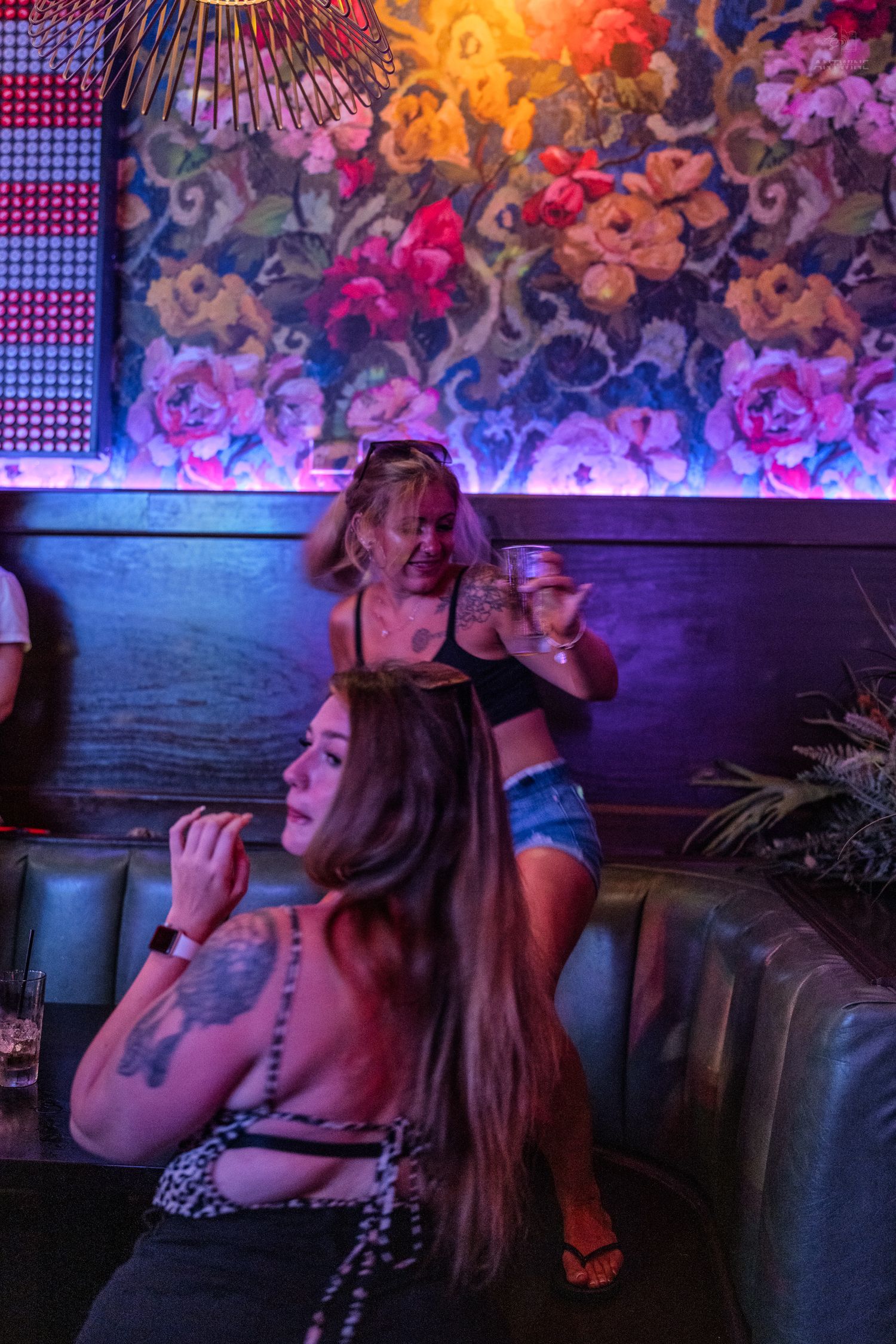 Women relaxing in booth seating under colorful floral mural in vibrant nightclub setting.