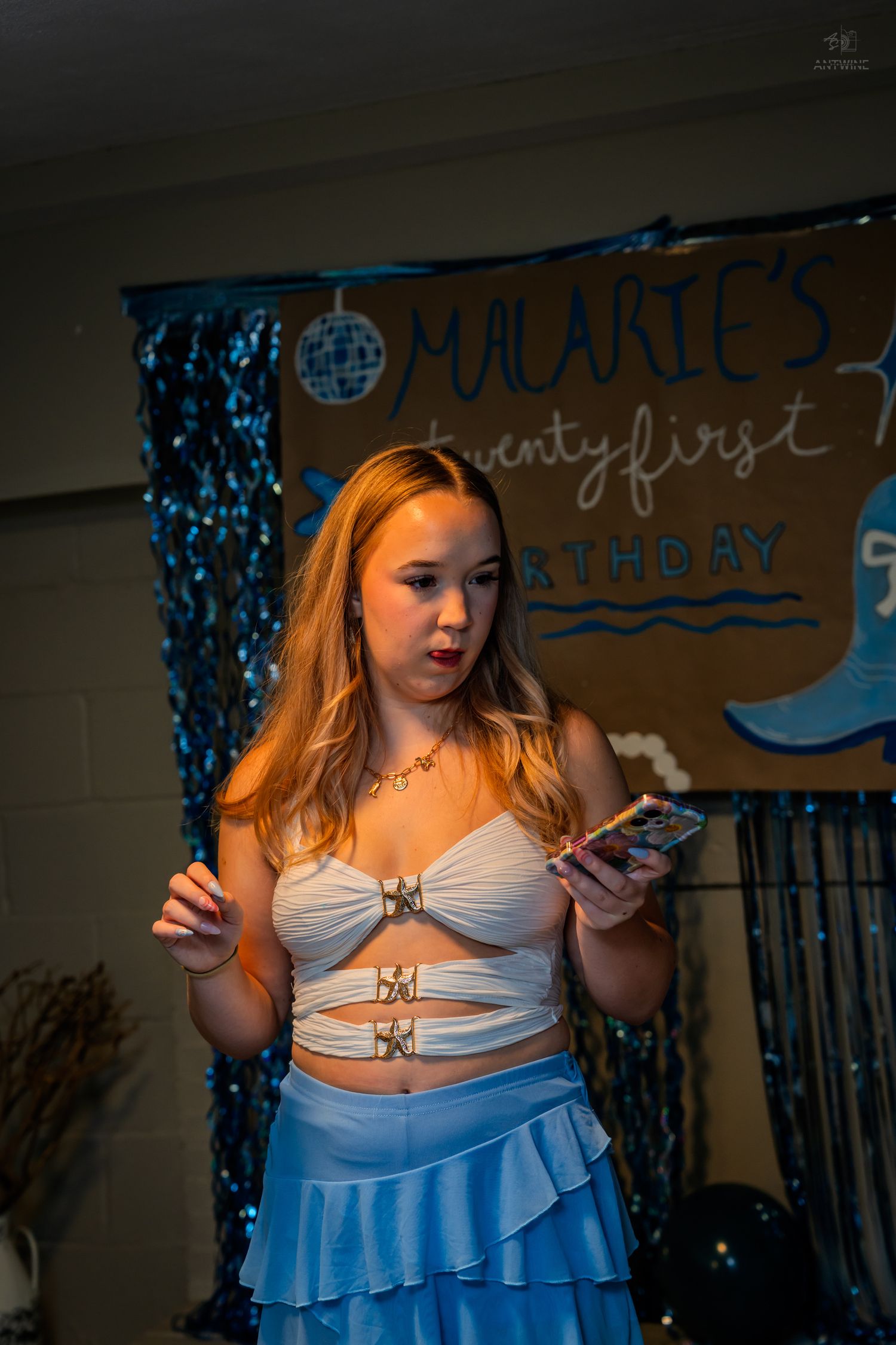 Young woman holding phone in blue ruffled skirt at Malarie's twentyfirst birthday party backdrop.