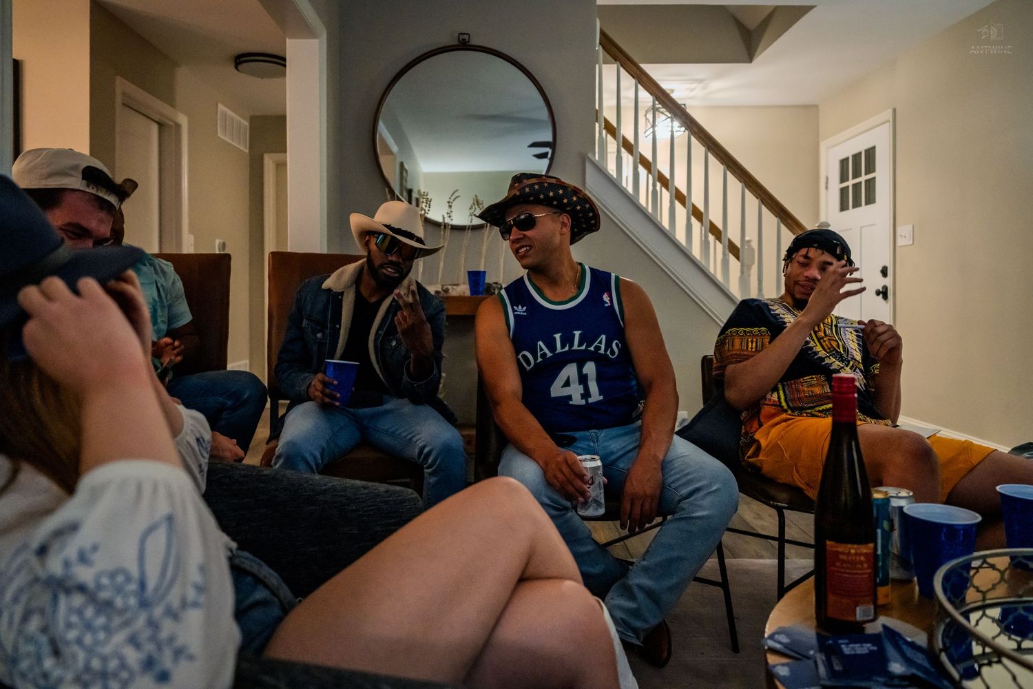 Group of friends in cowboy hats relaxing in a living room with drinks.