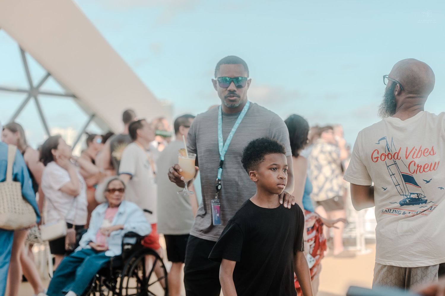 Man and child walking through a crowd on a sunny cruise ship deck.