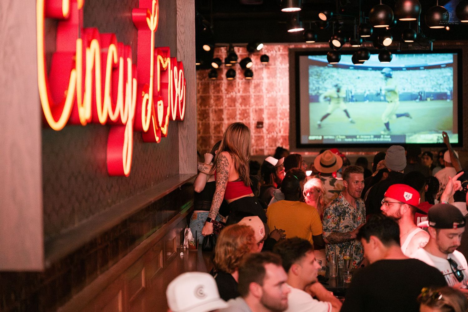 Lively sports bar with Cincy Lives neon sign, patrons watching soccer on large screen TV.