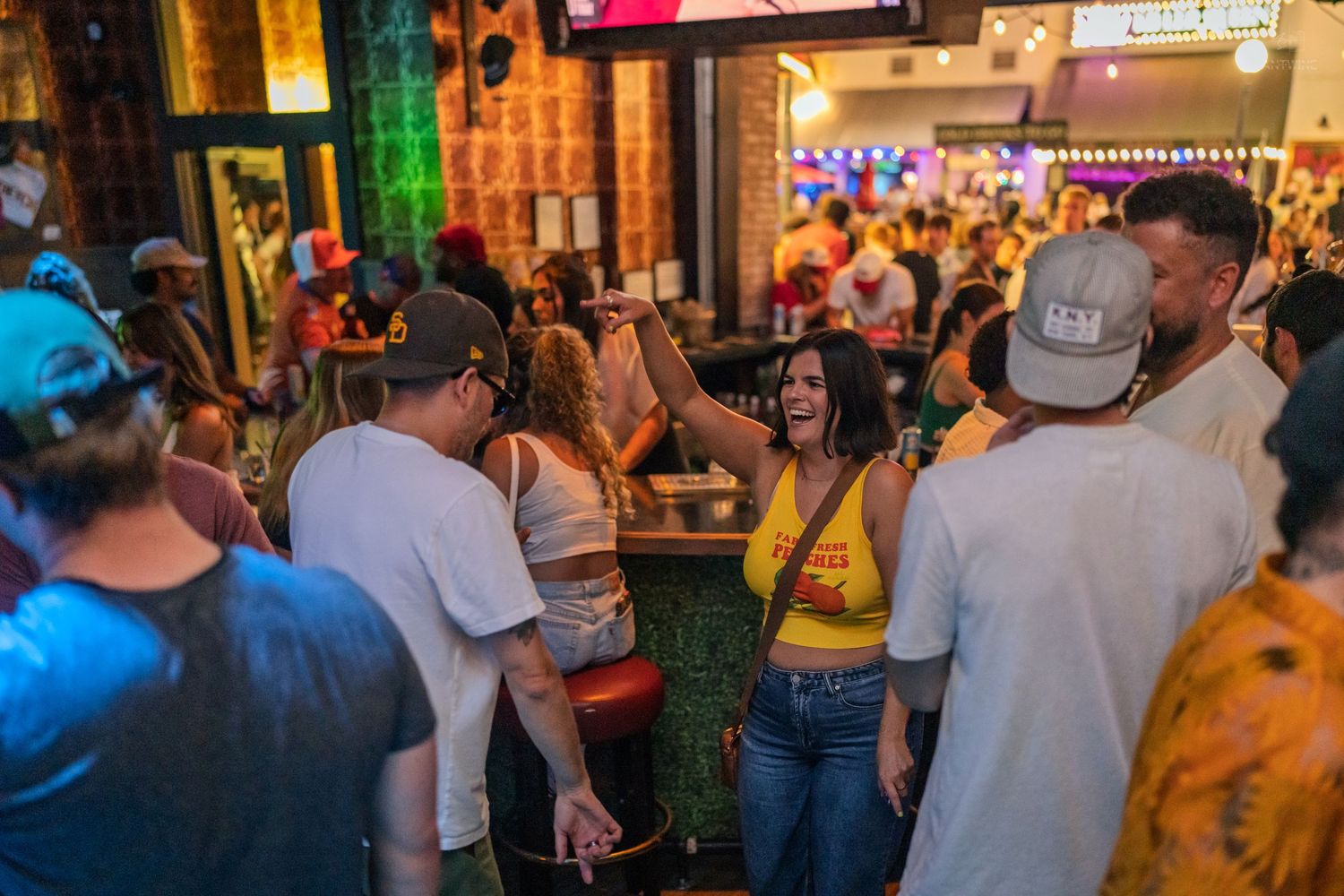Lively crowd dancing and socializing inside a packed bar with colorful neon lighting.