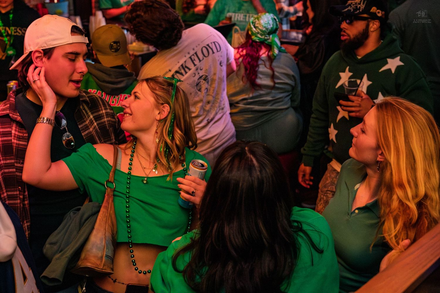 Women in green outfits chatting and drinking at a St. Patrick's Day bar celebration.