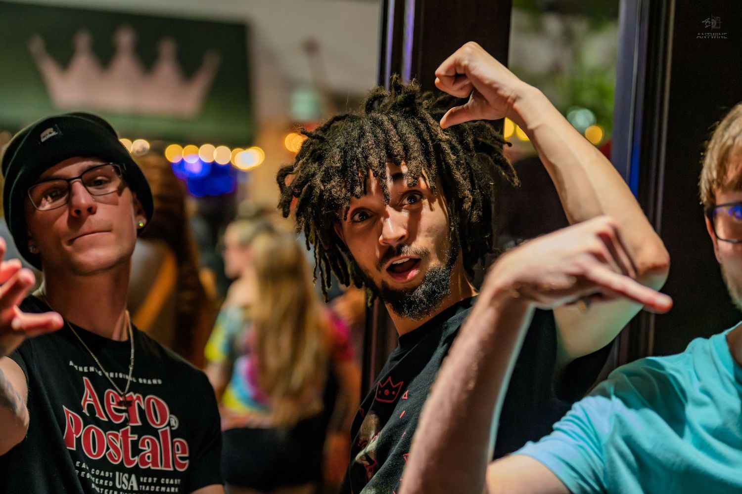 Three young men posing energetically inside a colorful nightlife venue.