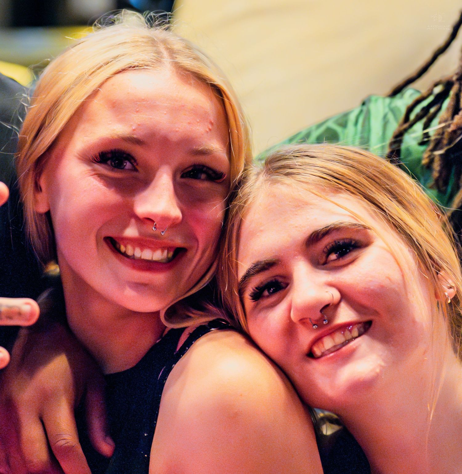 Two young blonde women smiling and posing cheek to cheek at a social event.