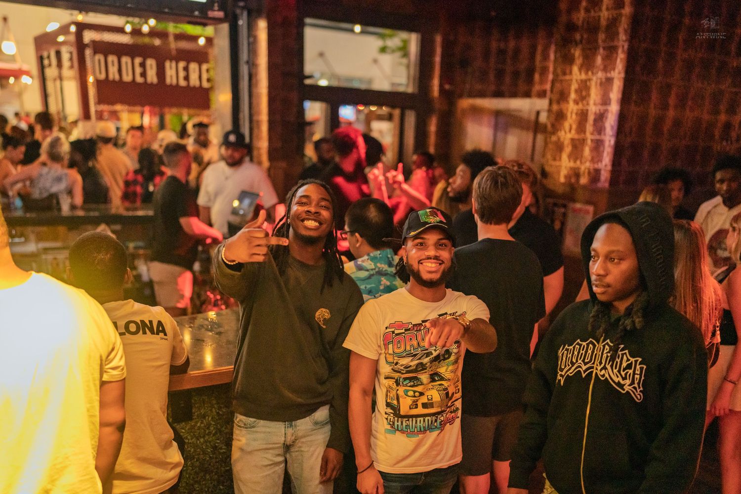 Three friends smiling and posing with peace sign in a packed nightclub venue at night.