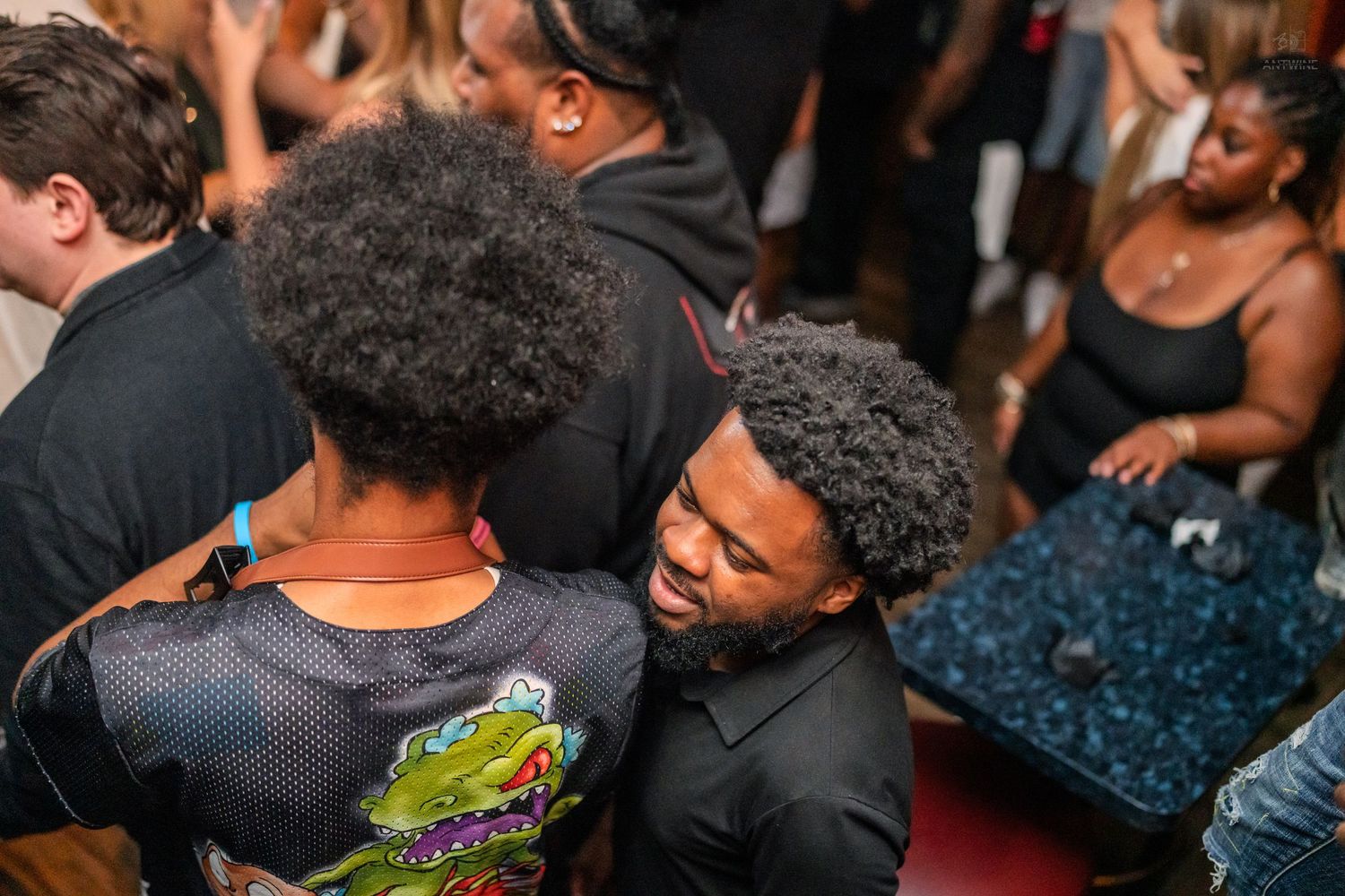 Friends embracing and socializing on a red carpet at a packed nightclub event.