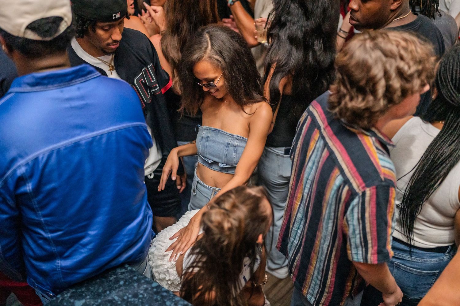 Young woman in denim outfit dancing in a packed nightclub crowd under dim ambient lighting.