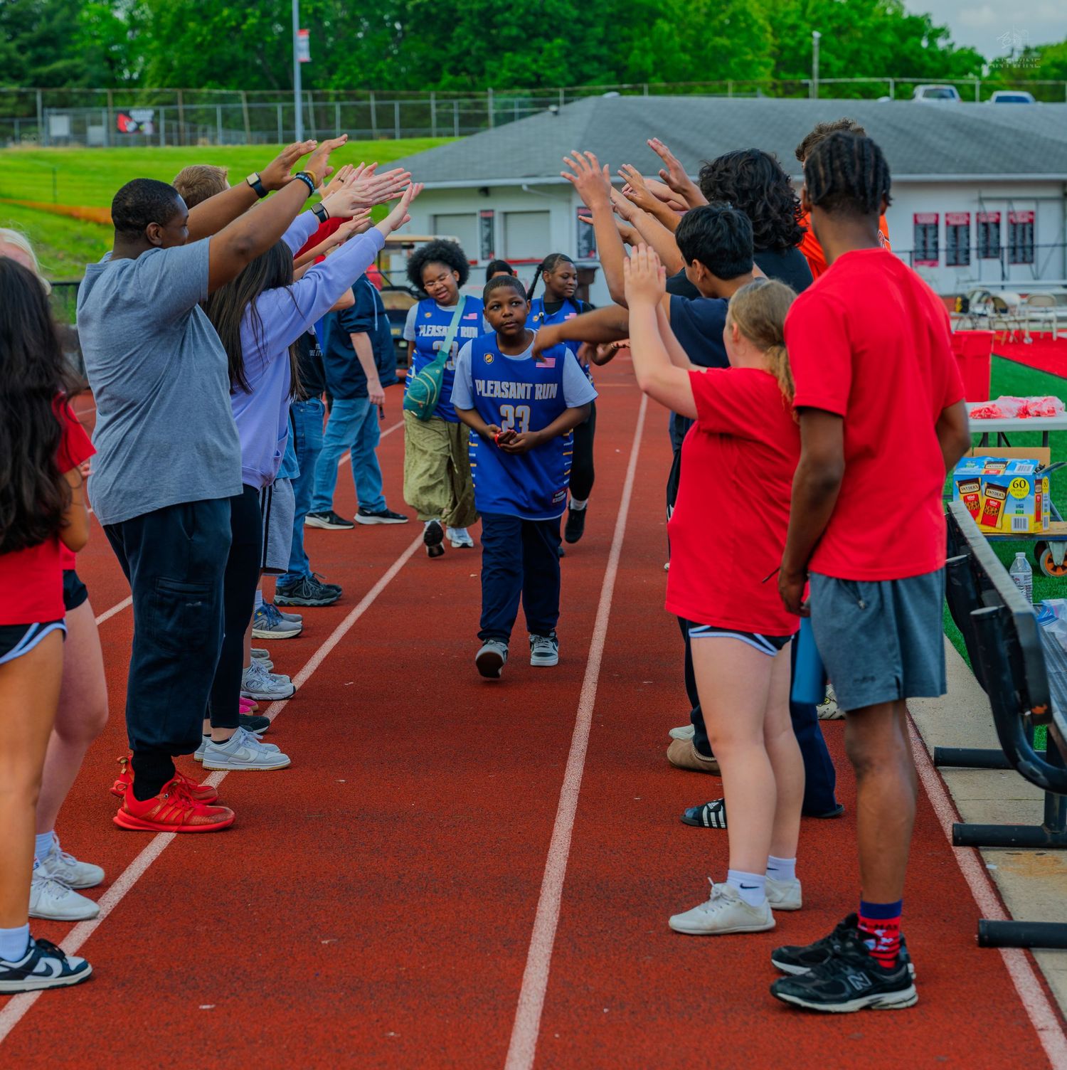 Athletes high-five participants running through a celebratory tunnel on an outdoor track at a school sports event.
