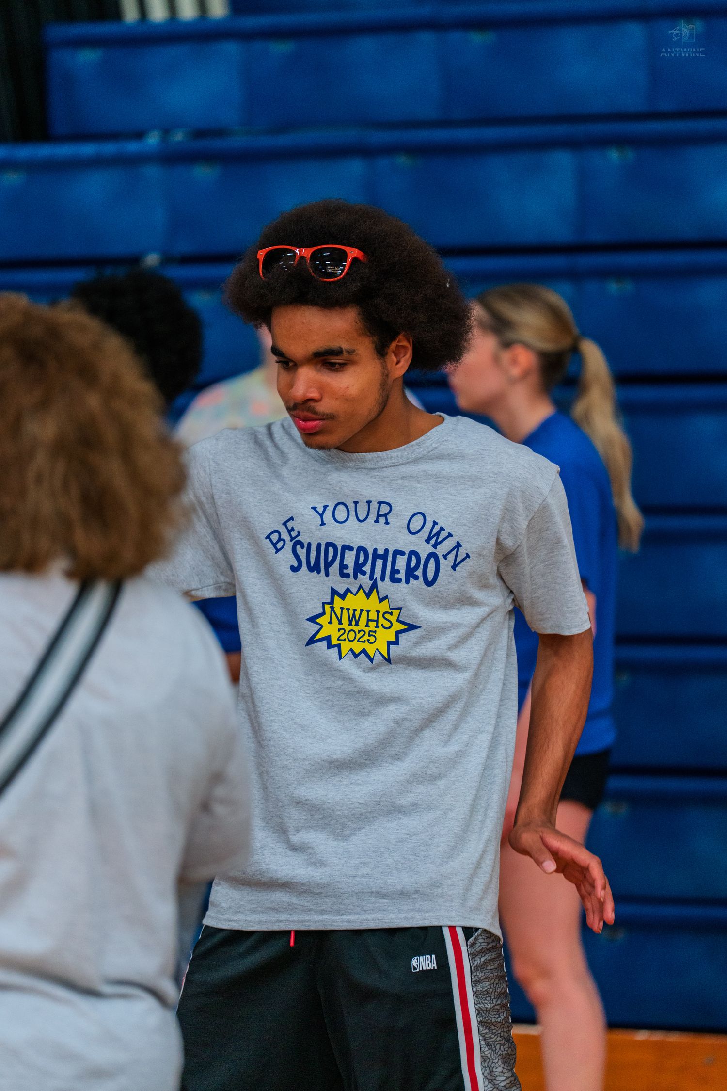 Teen wearing a Be Your Own Superhero NWHS 2022 gray t-shirt with red sunglasses in a school gymnasium.