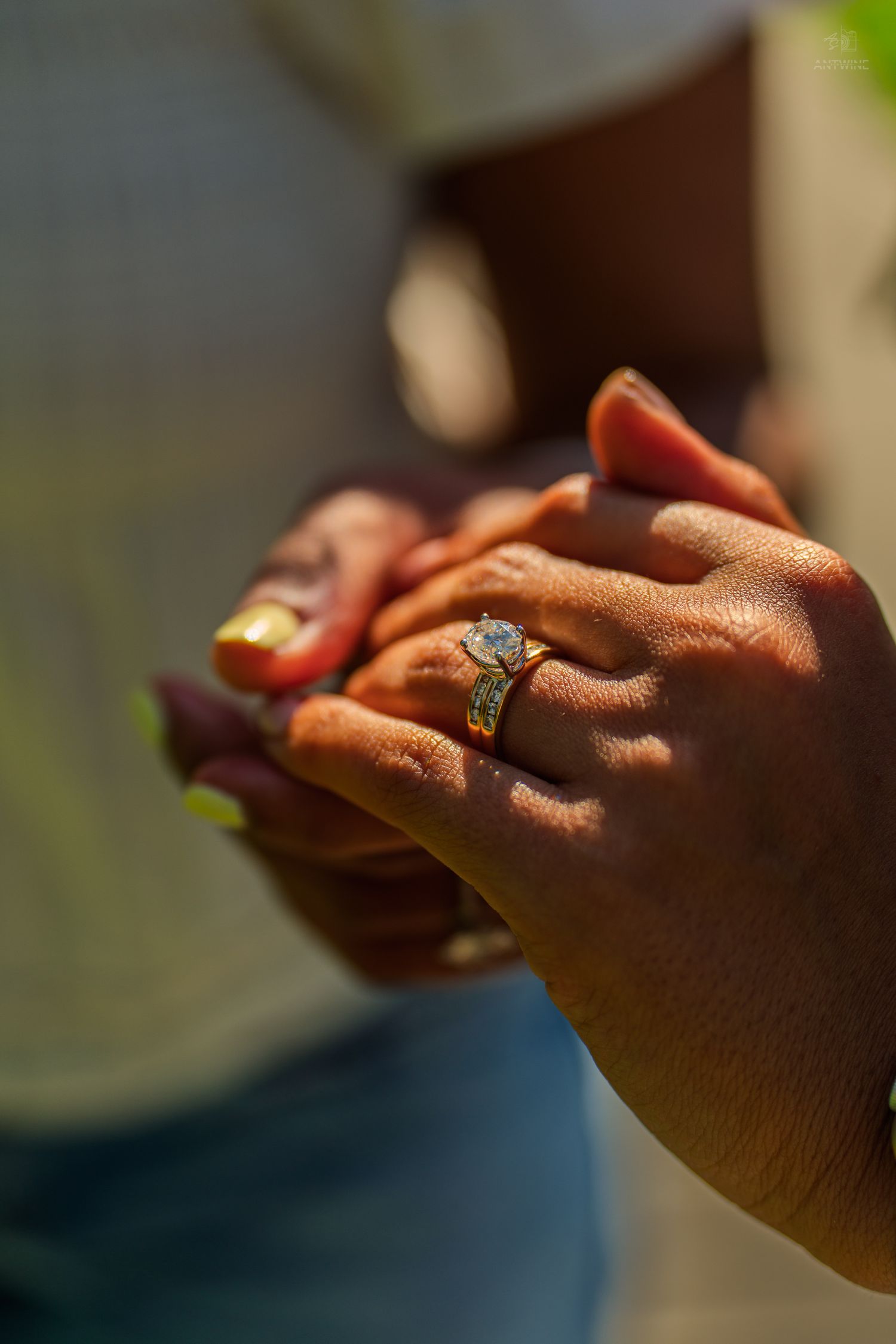 Close-up of two hands holding together displaying a gold diamond engagement ring in sunlight.