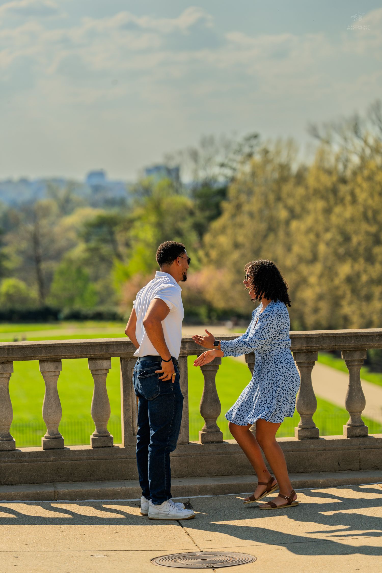 Happy couple standing together on a stone balustrade terrace surrounded by lush green parkland.