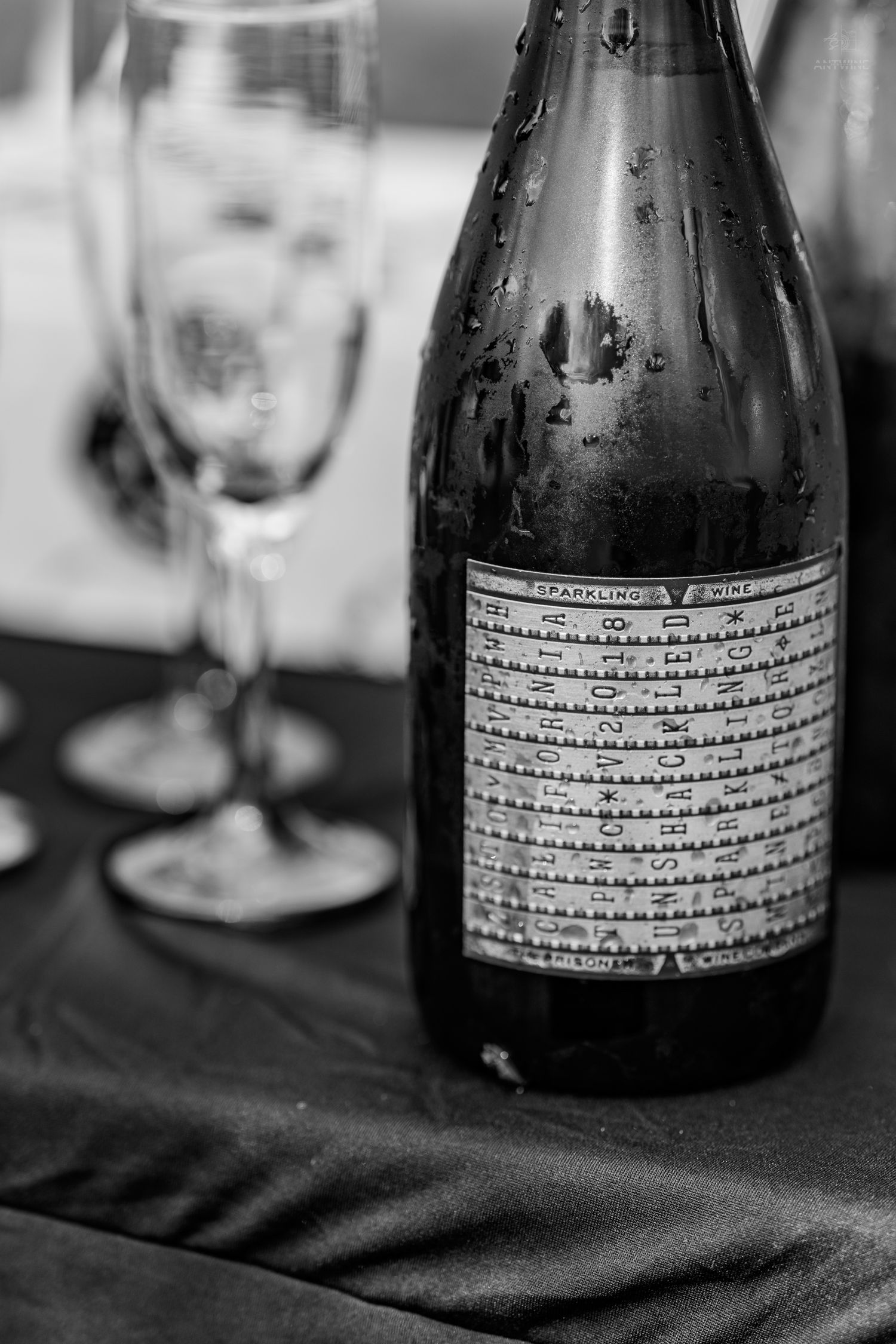 Close-up of a sparkling wine bottle with condensation next to champagne flutes on a black surface.