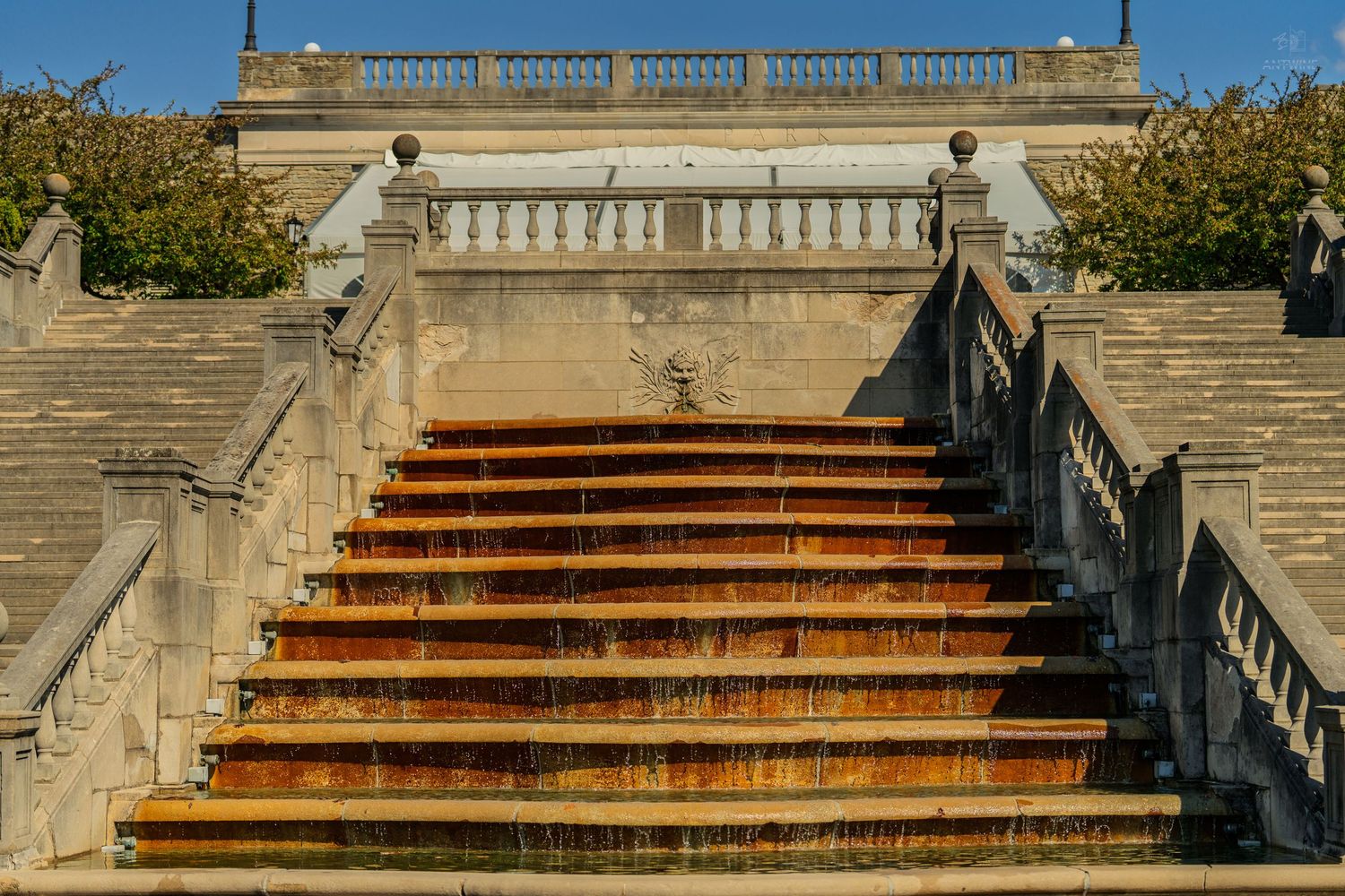 Sunlit stone cascade staircase with rust-stained steps and elegant balustrade railing at a classical landmark.