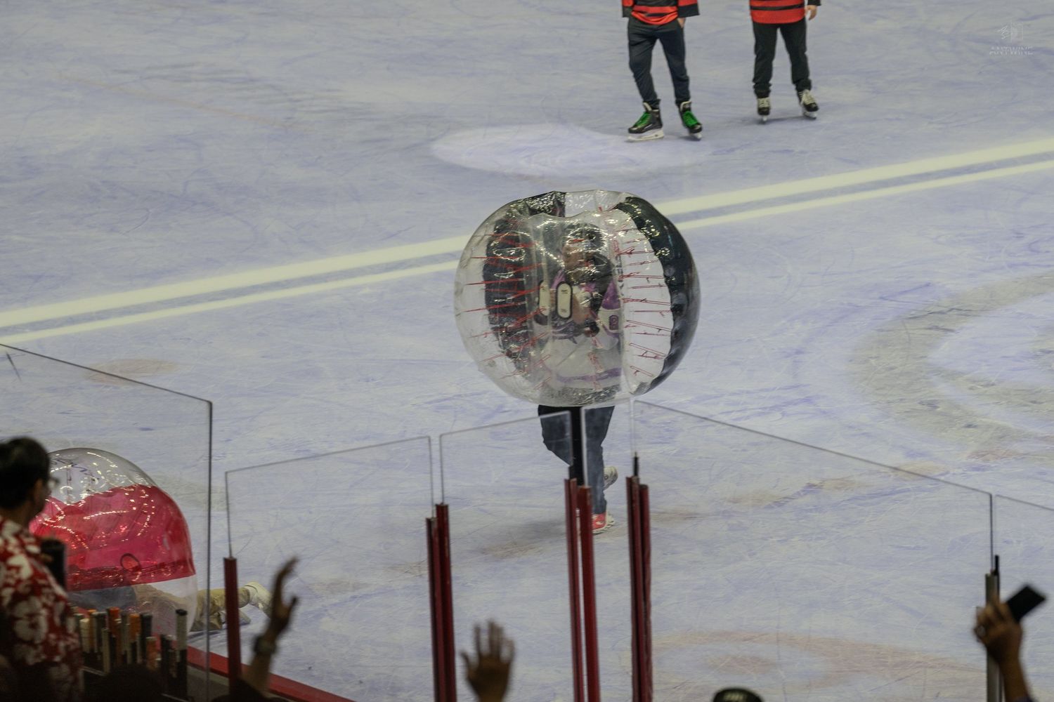 A person inside a large transparent inflatable zorb ball plays bubble soccer on an ice rink.