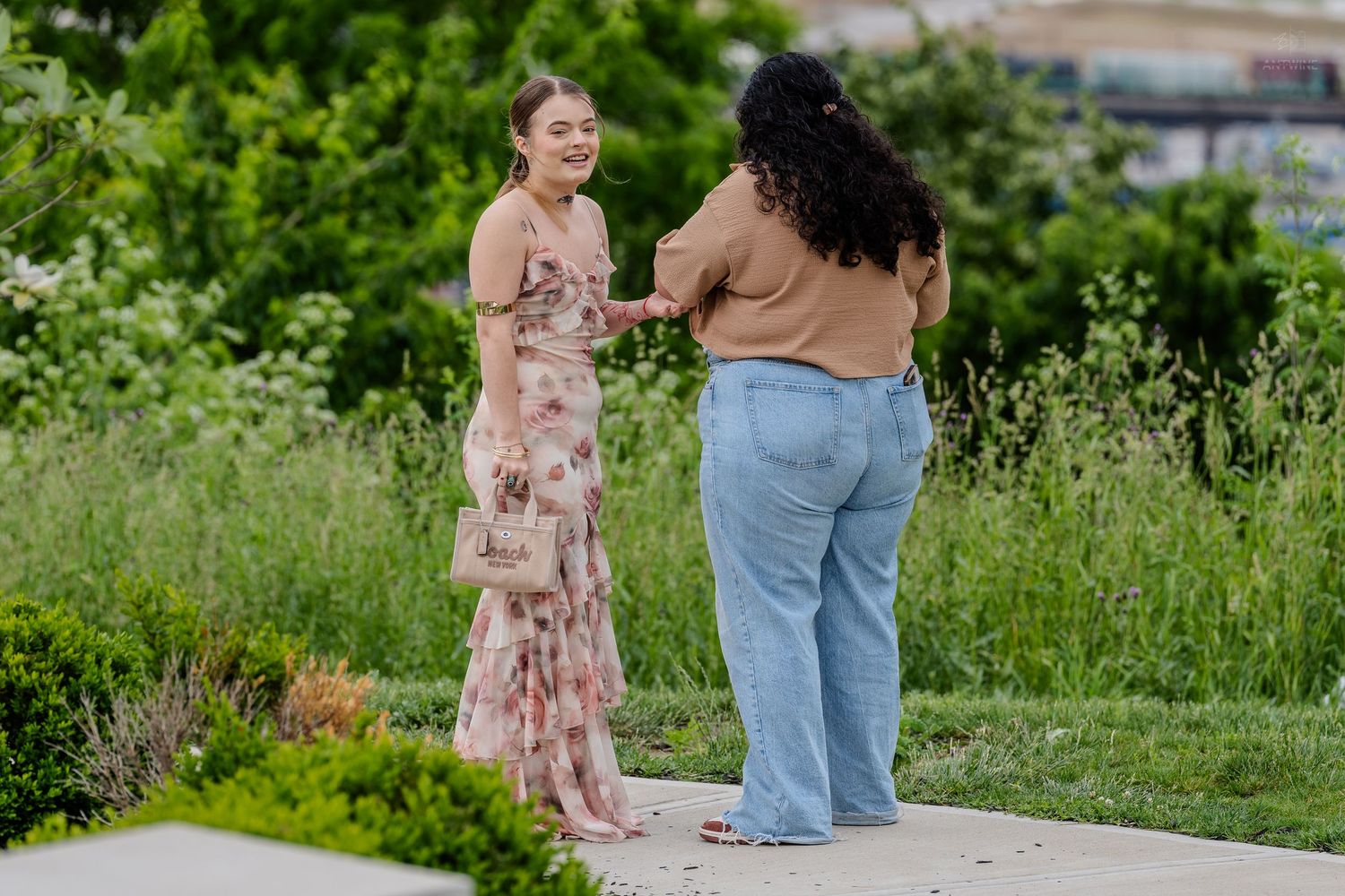 Woman in floral maxi dress laughing joyfully during outdoor engagement moment with green landscape.
