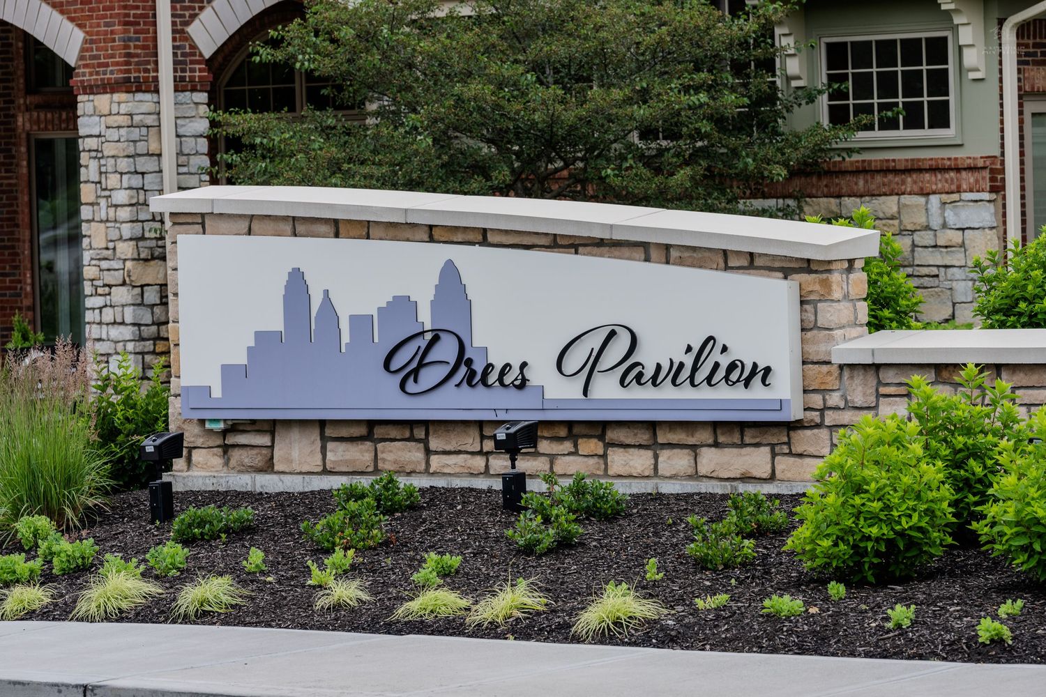Drees Pavilion entrance sign with Cincinnati skyline silhouette surrounded by green landscaping.