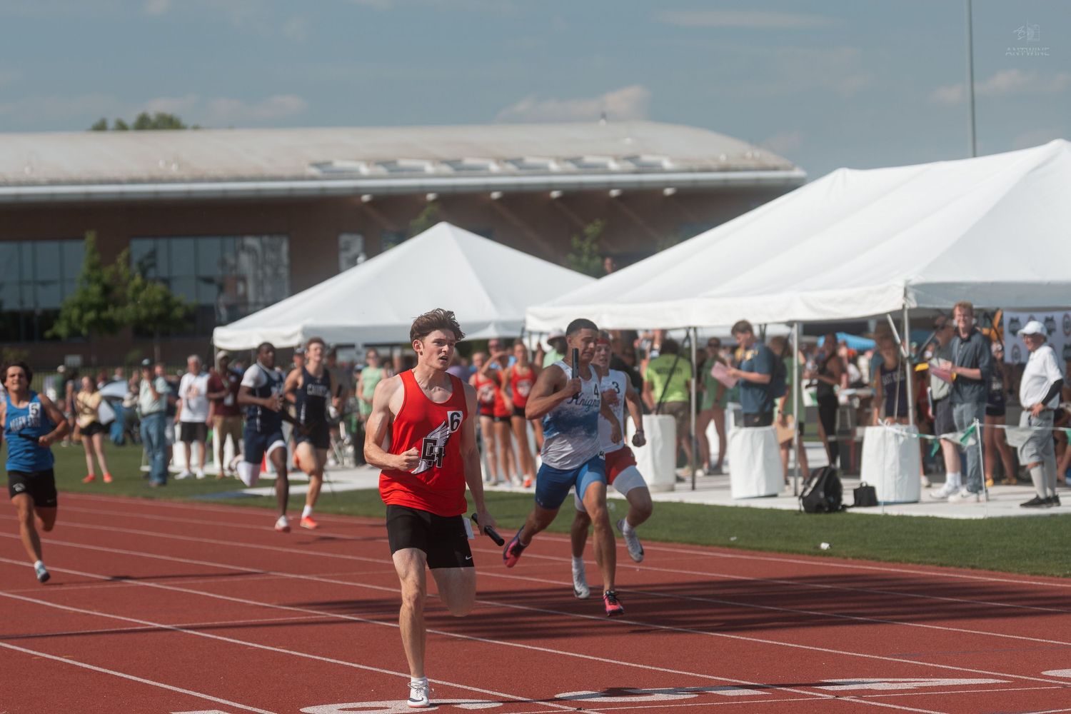 Young athlete in red uniform leads a sprint race at an outdoor high school track and field meet.