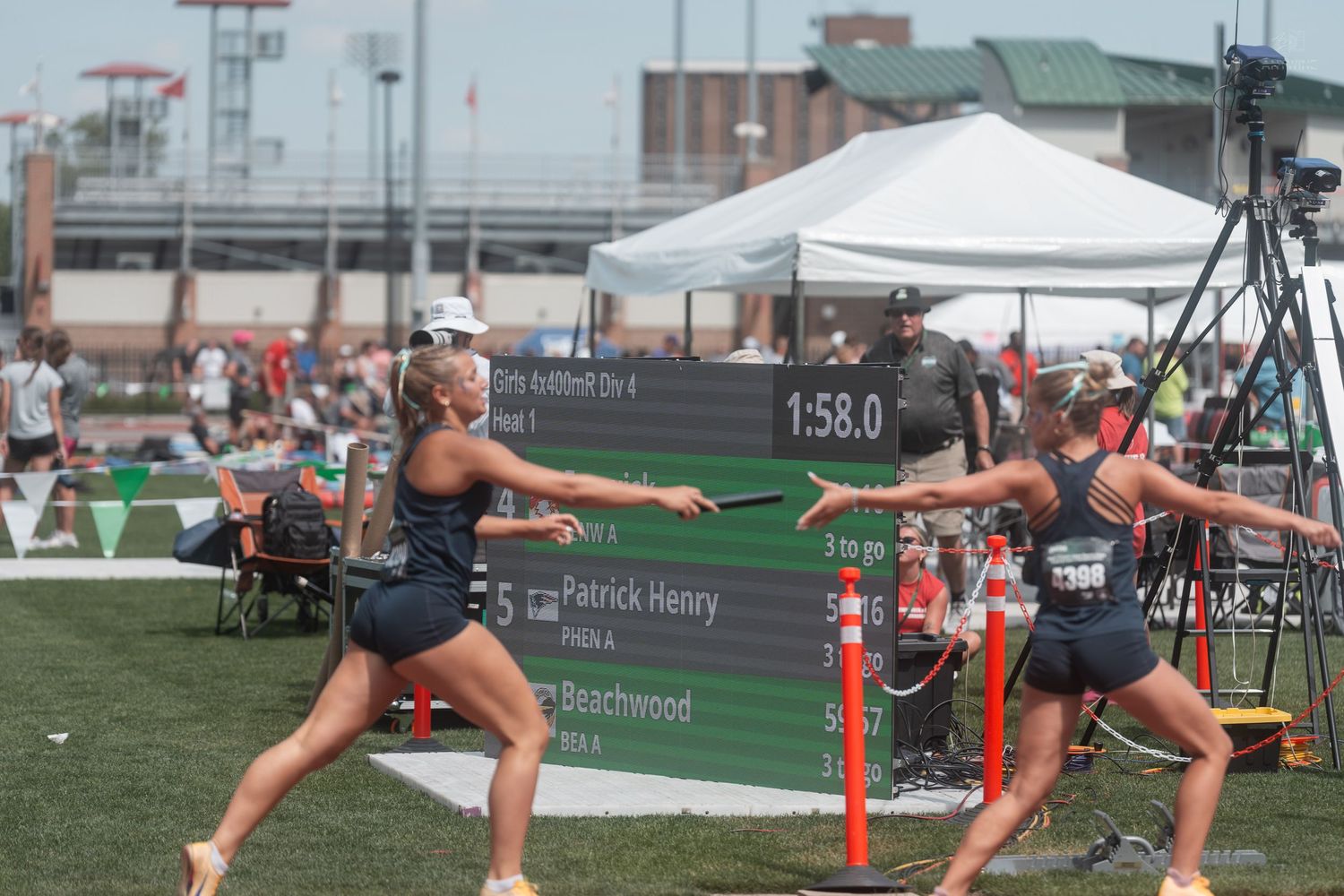 Two female relay runners exchange a baton on a track during a competitive high school state championship race.