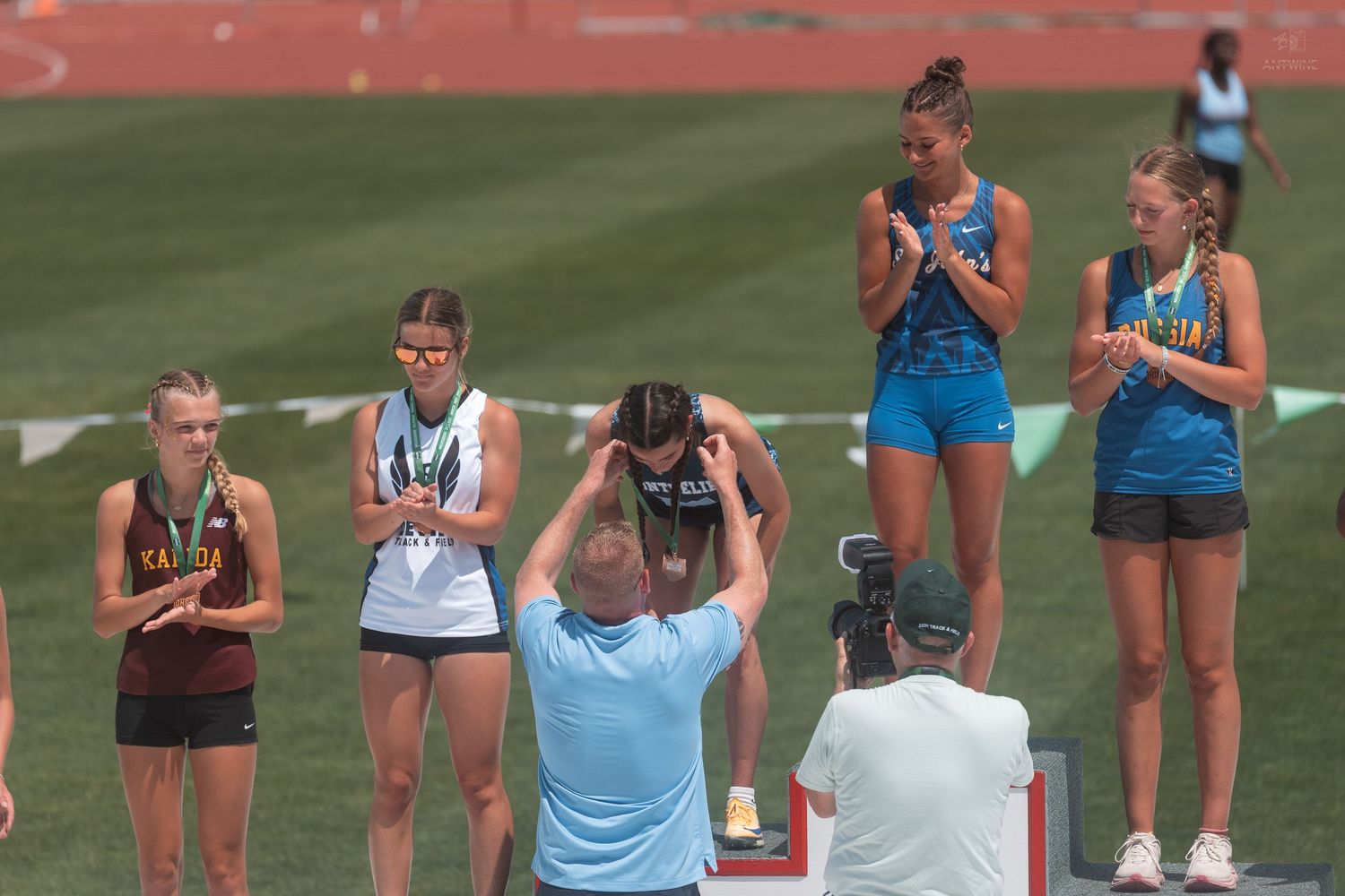 Female track athletes receive medals at OHSAA state championship awards ceremony on sunny day.