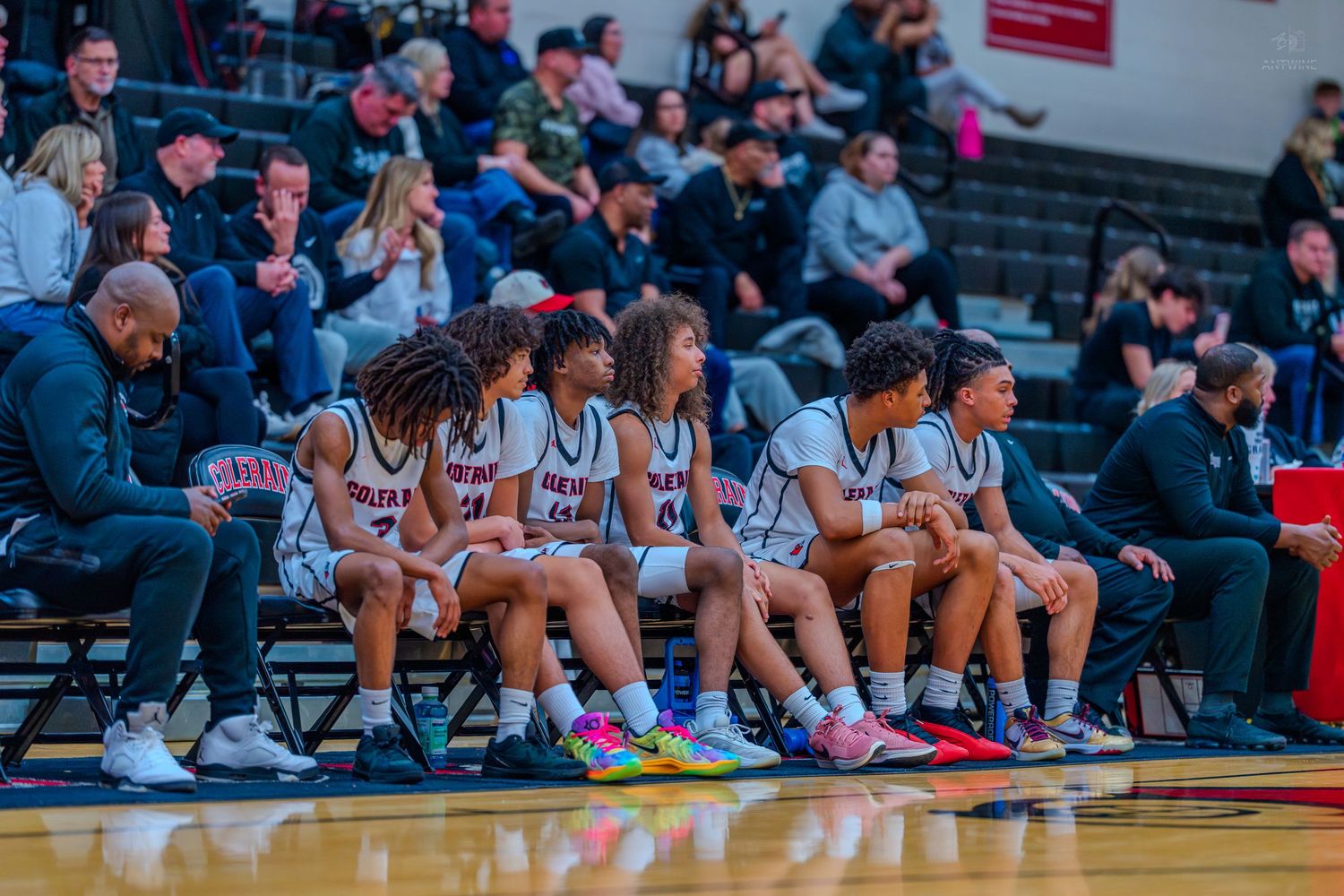 Colerain high school basketball team sits on the bench during a game in white uniforms.