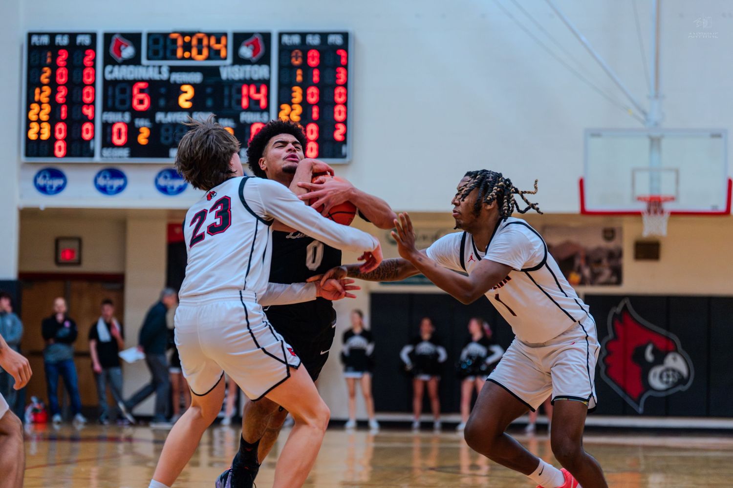 Two Cardinals basketball players double-team an opponent during a high school basketball game with scoreboard showing 7:04.