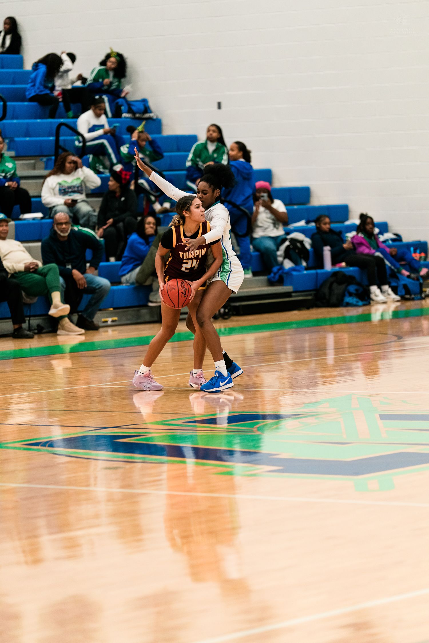 A female basketball player in a brown Turpin jersey shields the ball while a defender reaches over her during a high school game.