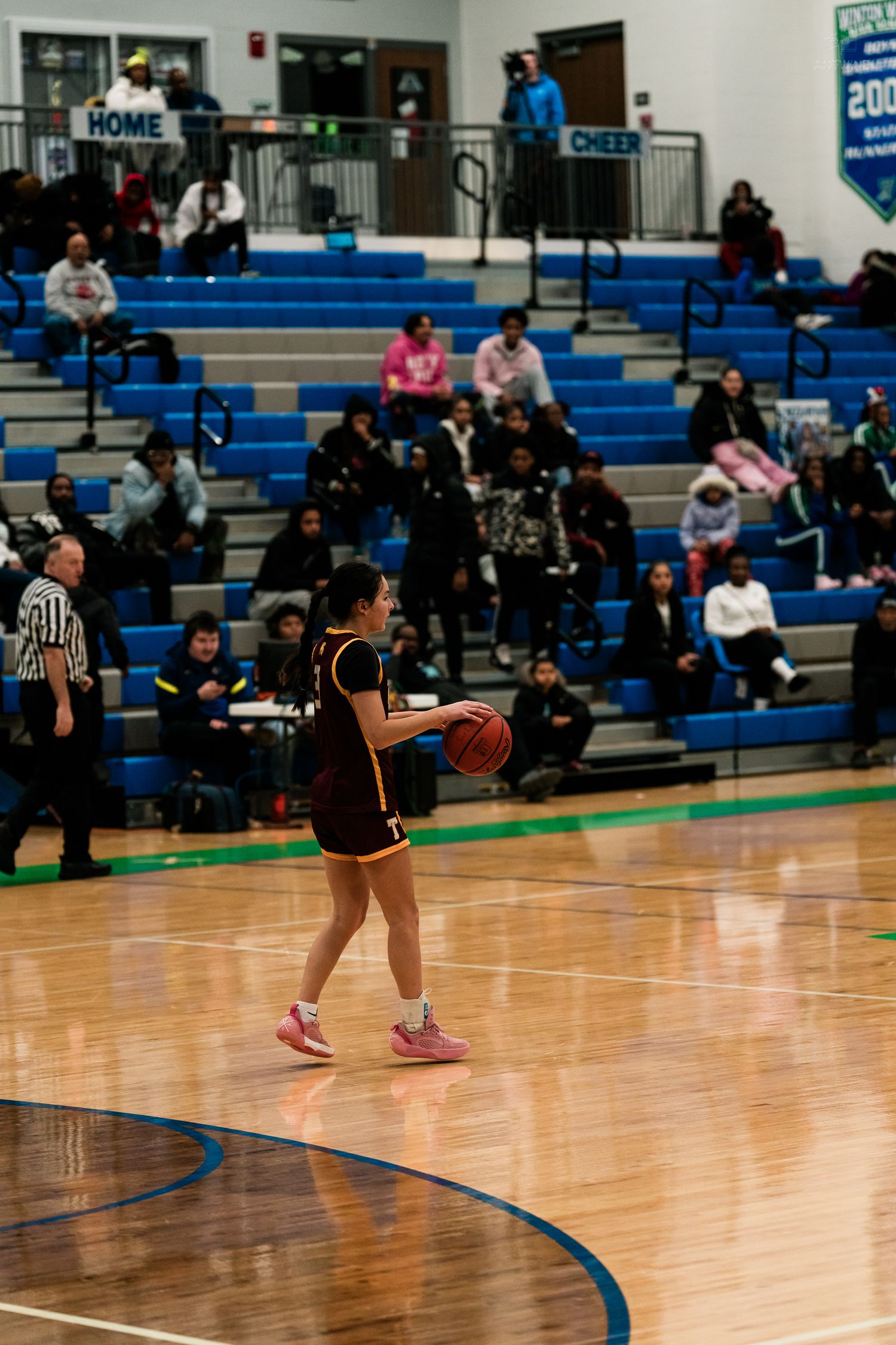 A girls basketball player in maroon dribbles the ball during a high school game in a blue gymnasium.
