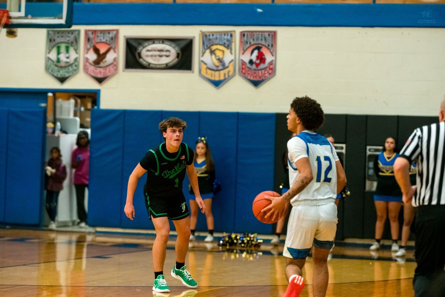Green-uniformed defender guards dribbling player in blue jersey on basketball court.