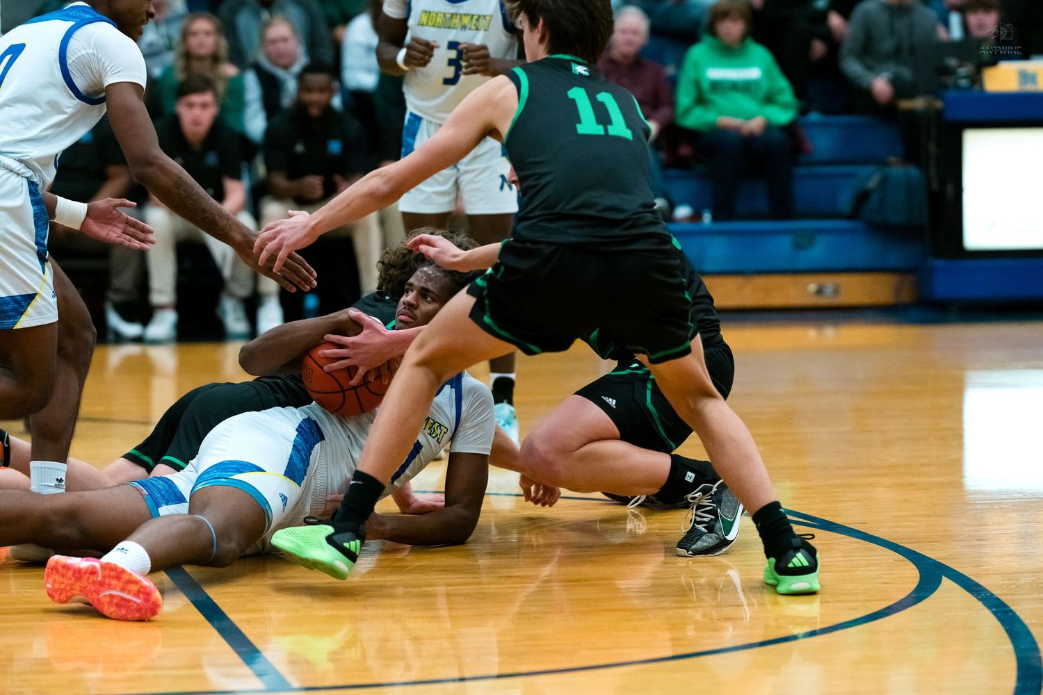 Basketball players scramble for a loose ball on the floor during a high school gymnasium game.
