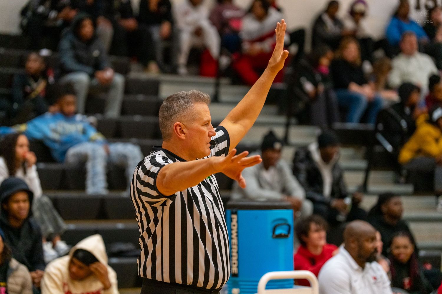 Basketball referee in black and white stripes signals call to players during high school game.
