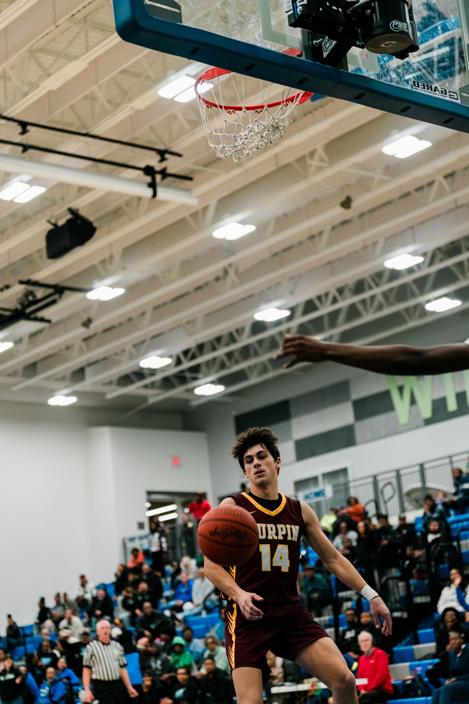 Turpin player number 14 goes up for a layup shot beneath the basketball hoop during a high school game.