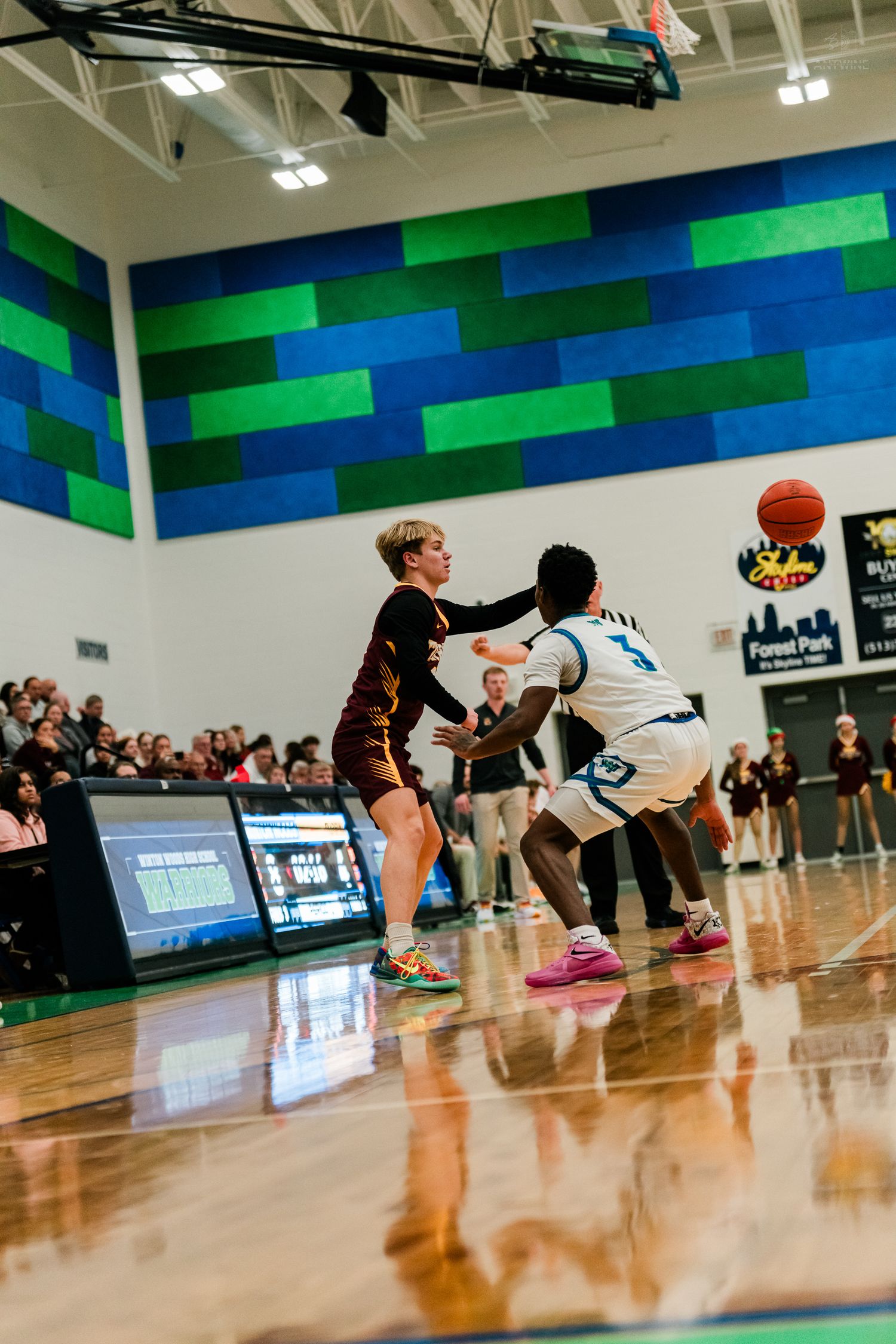 High school basketball player in maroon Turpin jersey defends against opponent during game at Forest Park gym.