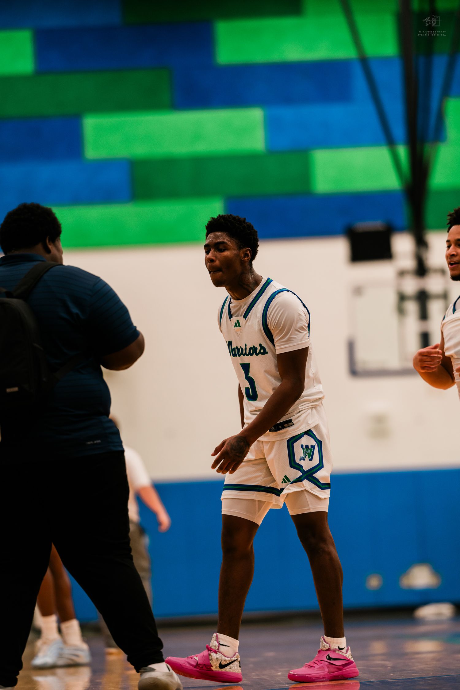 Warriors player number 3 smiles on the court during a high school basketball game with teammates nearby.