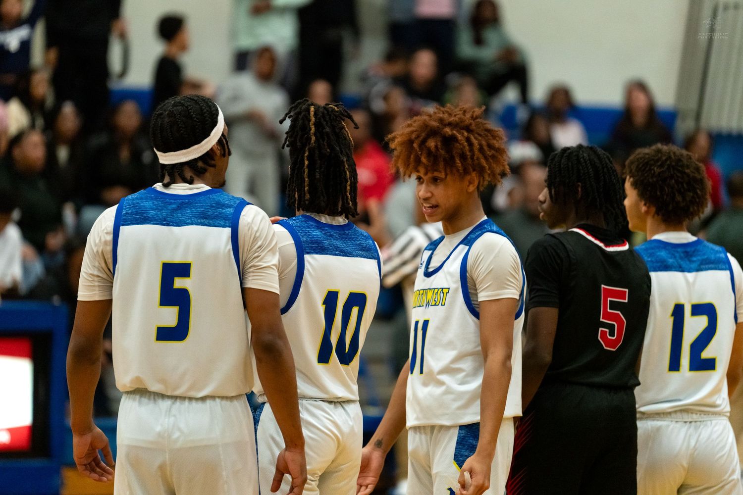 Northwest Knights players wearing numbers 5, 10, 11, and 12 huddle with opposing team during a high school basketball game.