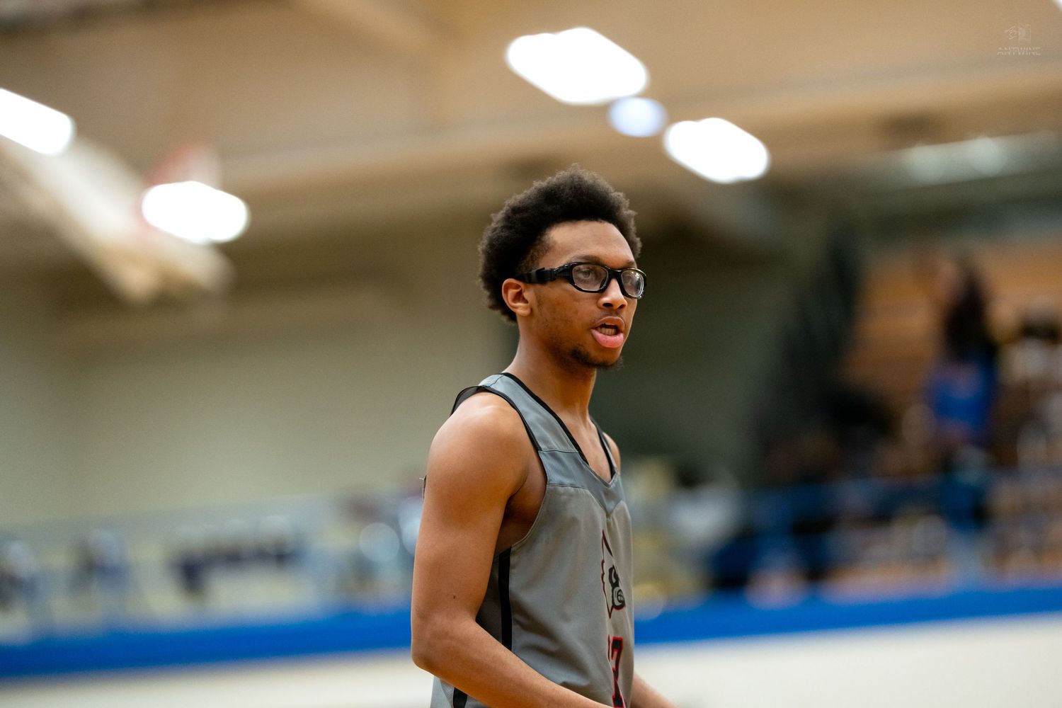 Basketball player wearing protective glasses and gray jersey stands on court during game.