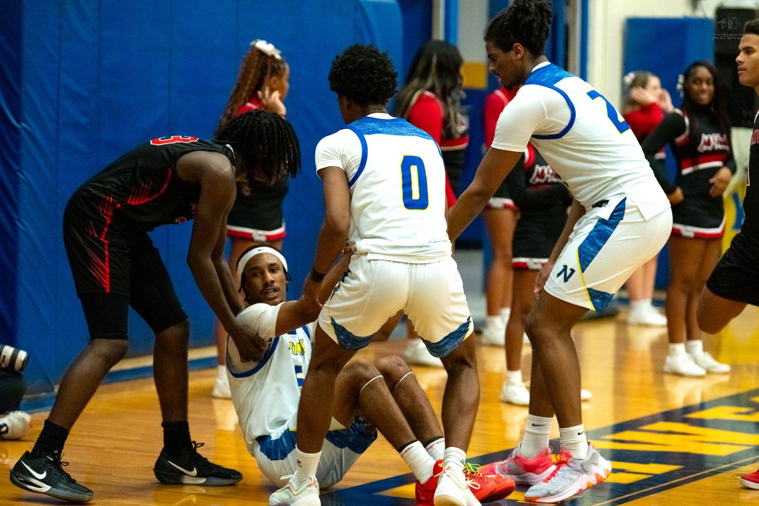 High school basketball player is helped up off the court by teammates in blue uniforms during a game.